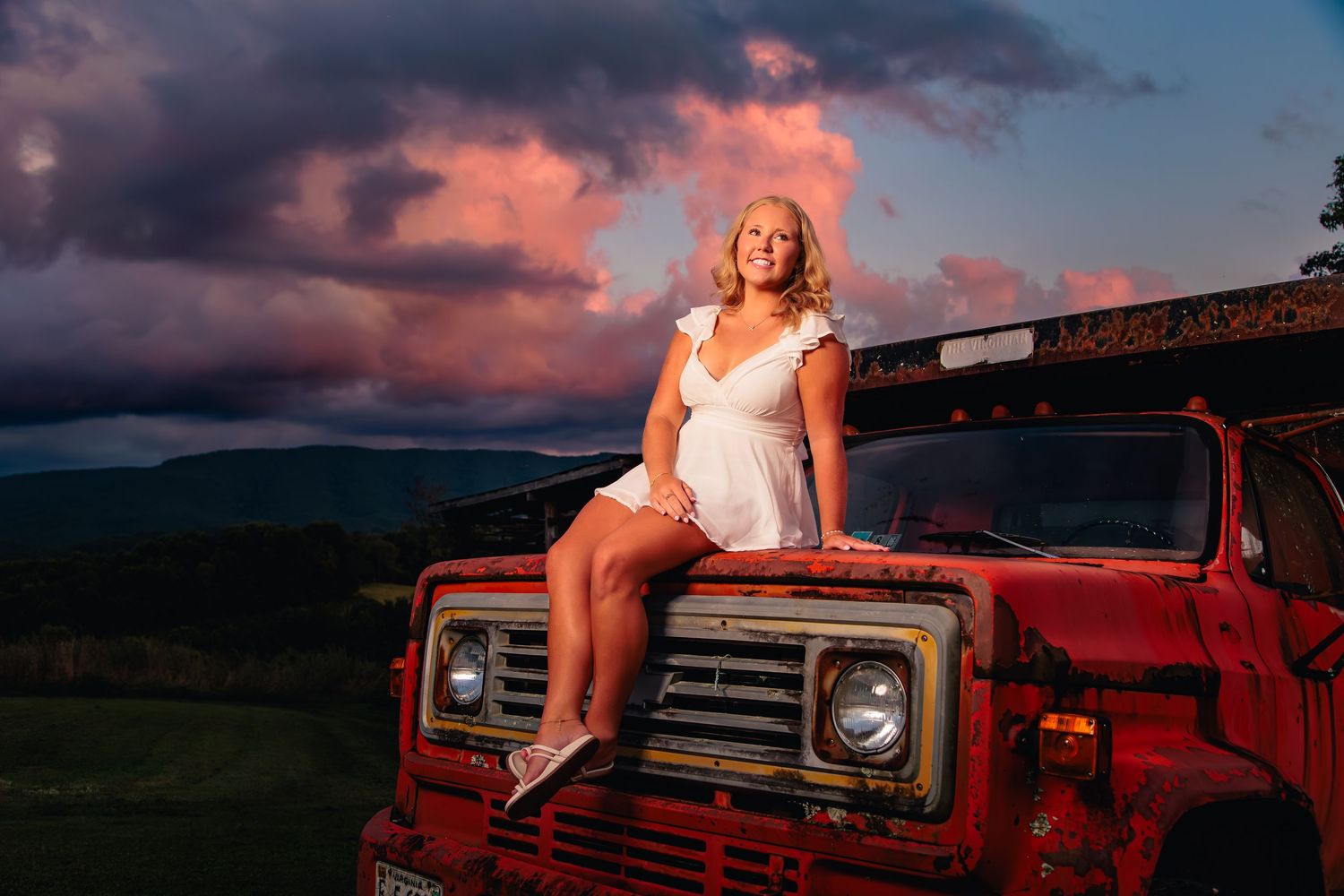 Vintage red truck parked against dramatic sunset sky with pink and purple clouds.