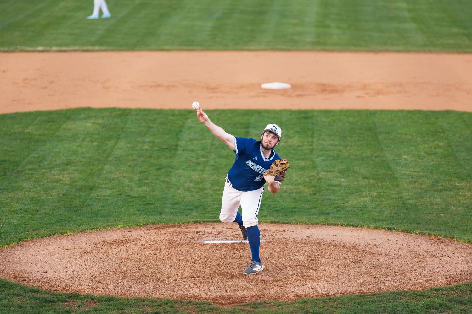 Baseball pitcher in blue uniform mid-throw on pitcher's mound during a game on a well-maintained field.