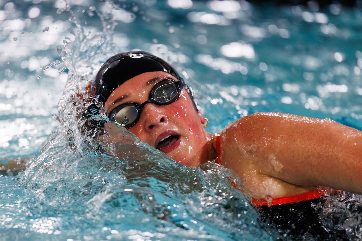 Swimmer performing freestyle technique in a pool with splashing water during competitive swimming event.