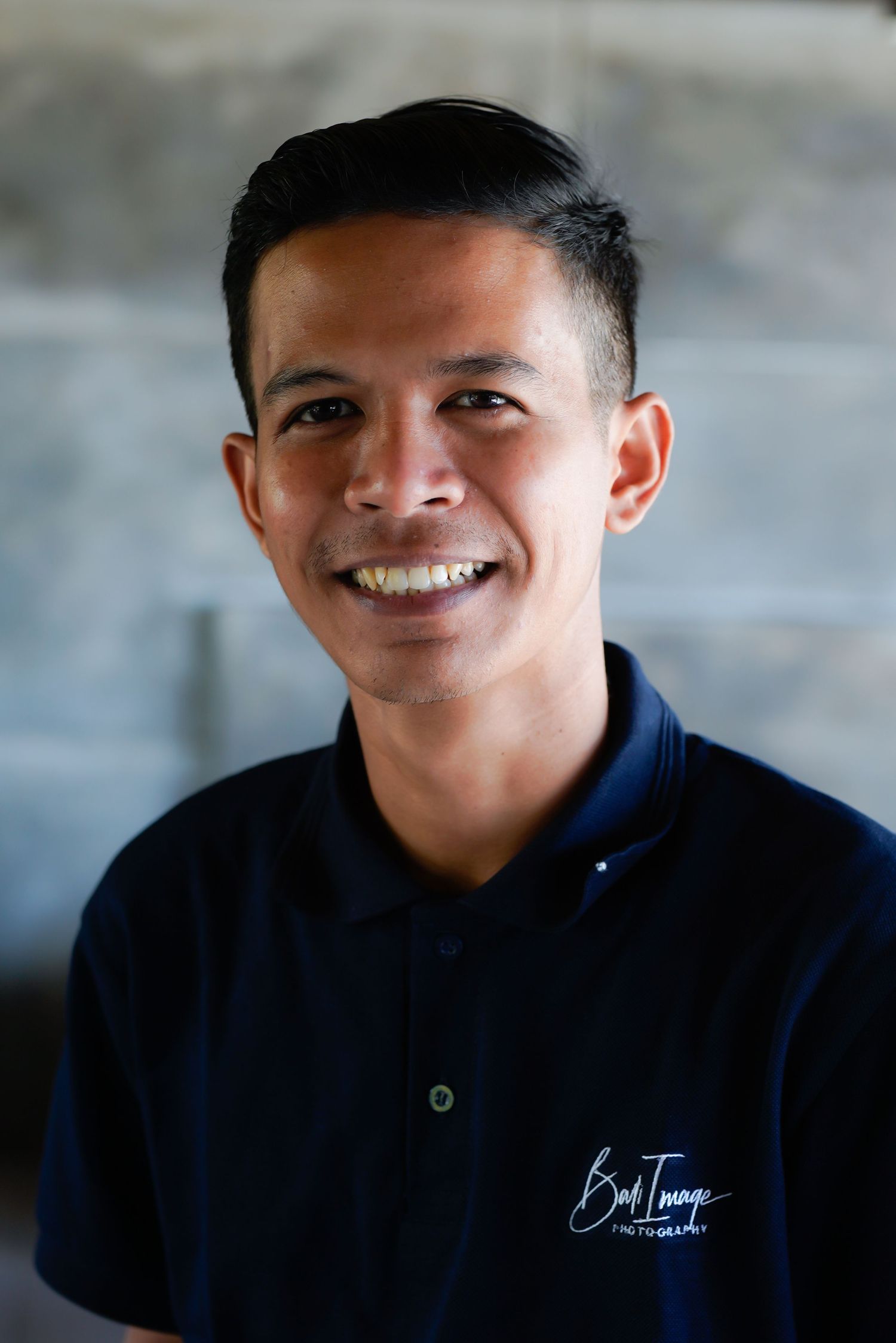 Staff member in navy polo shirt with Bali Towers logo smiles warmly at camera.