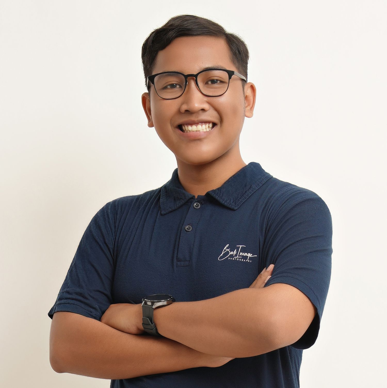 Professional wearing navy blue polo shirt and glasses poses with crossed arms against white background.
