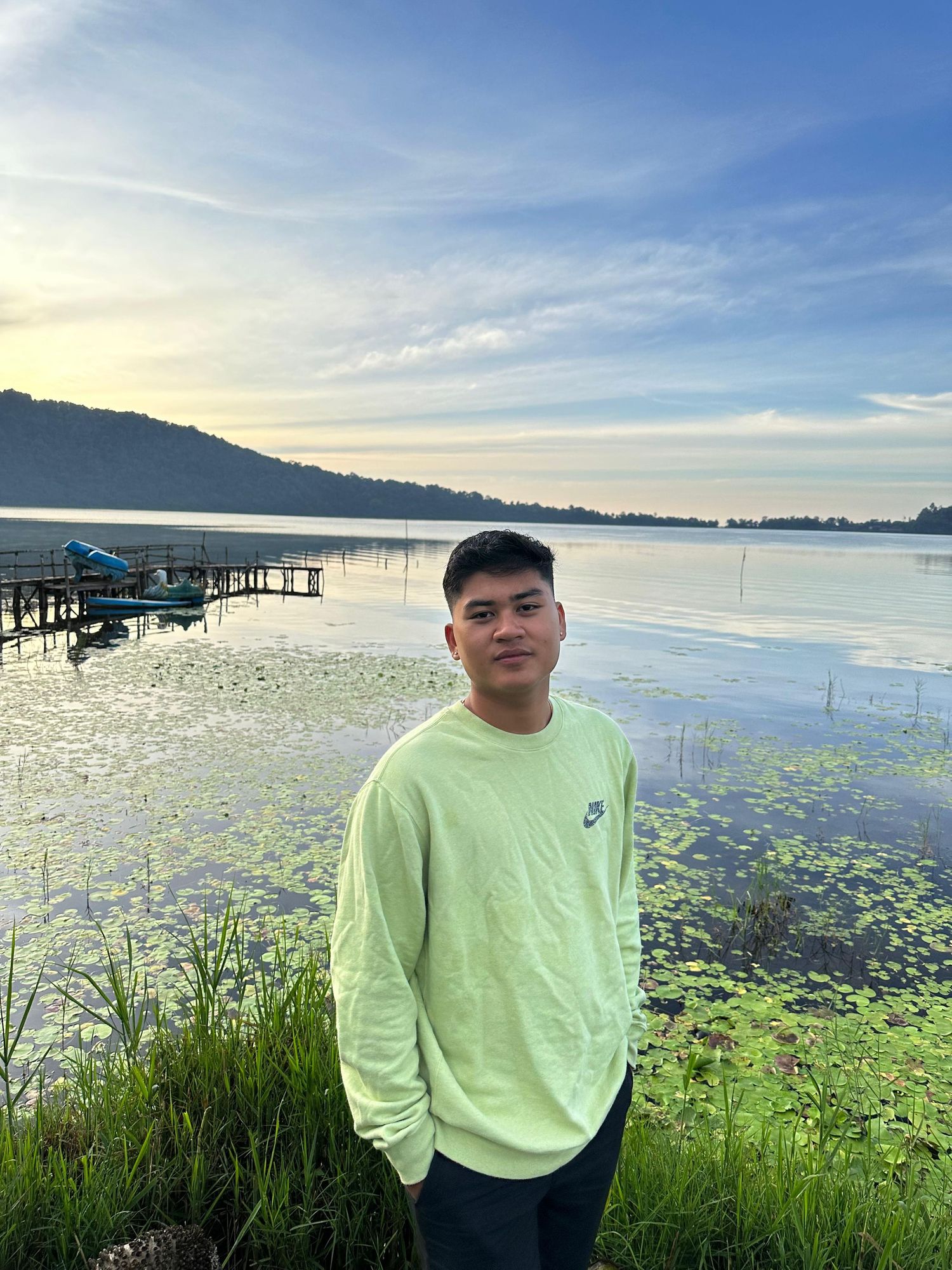 Person in light green sweatshirt standing by a serene lake with a dock at sunset.