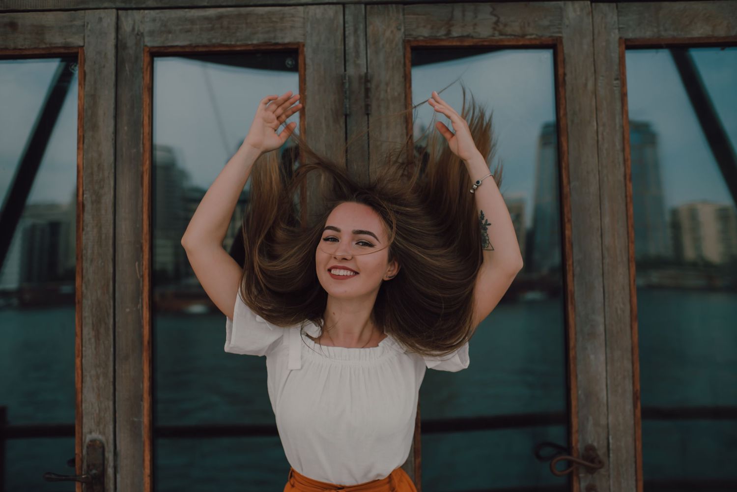 Woman in white dress poses joyfully near water with flowing hair in artistic photo series.