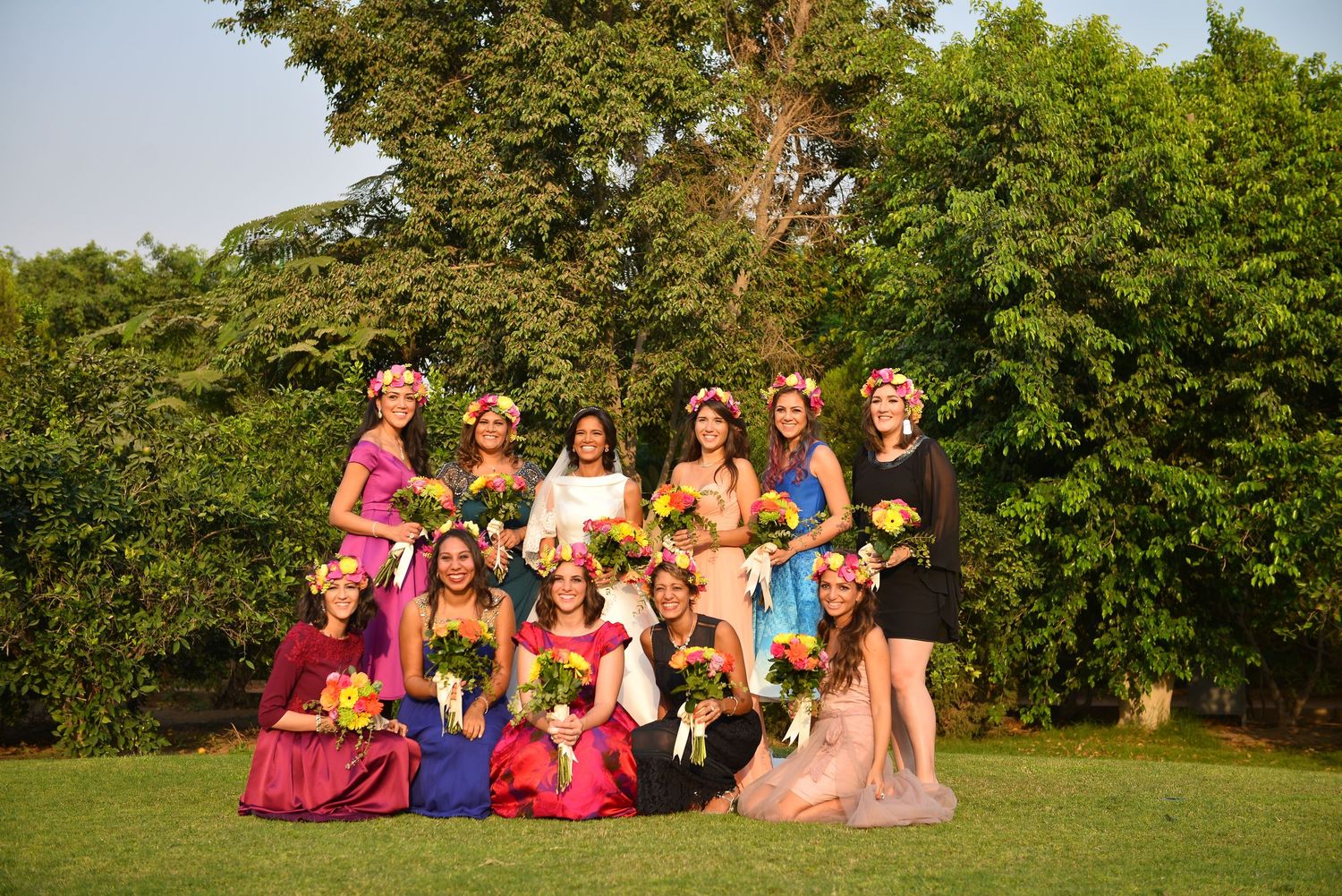 Wedding party members stand together in bright dresses against a natural outdoor backdrop.
