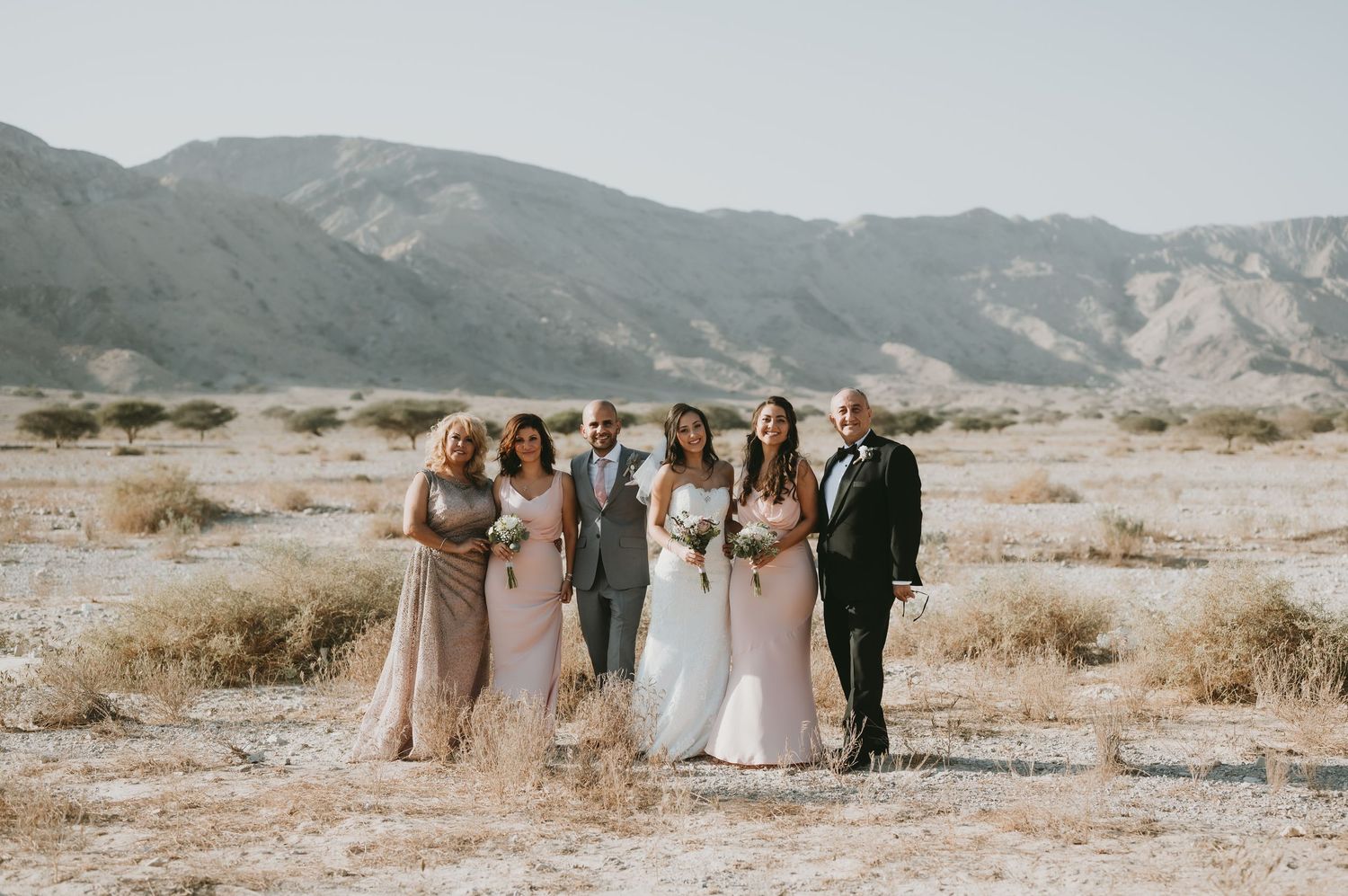 Wedding party poses in desert landscape with mountains in background during golden hour.
