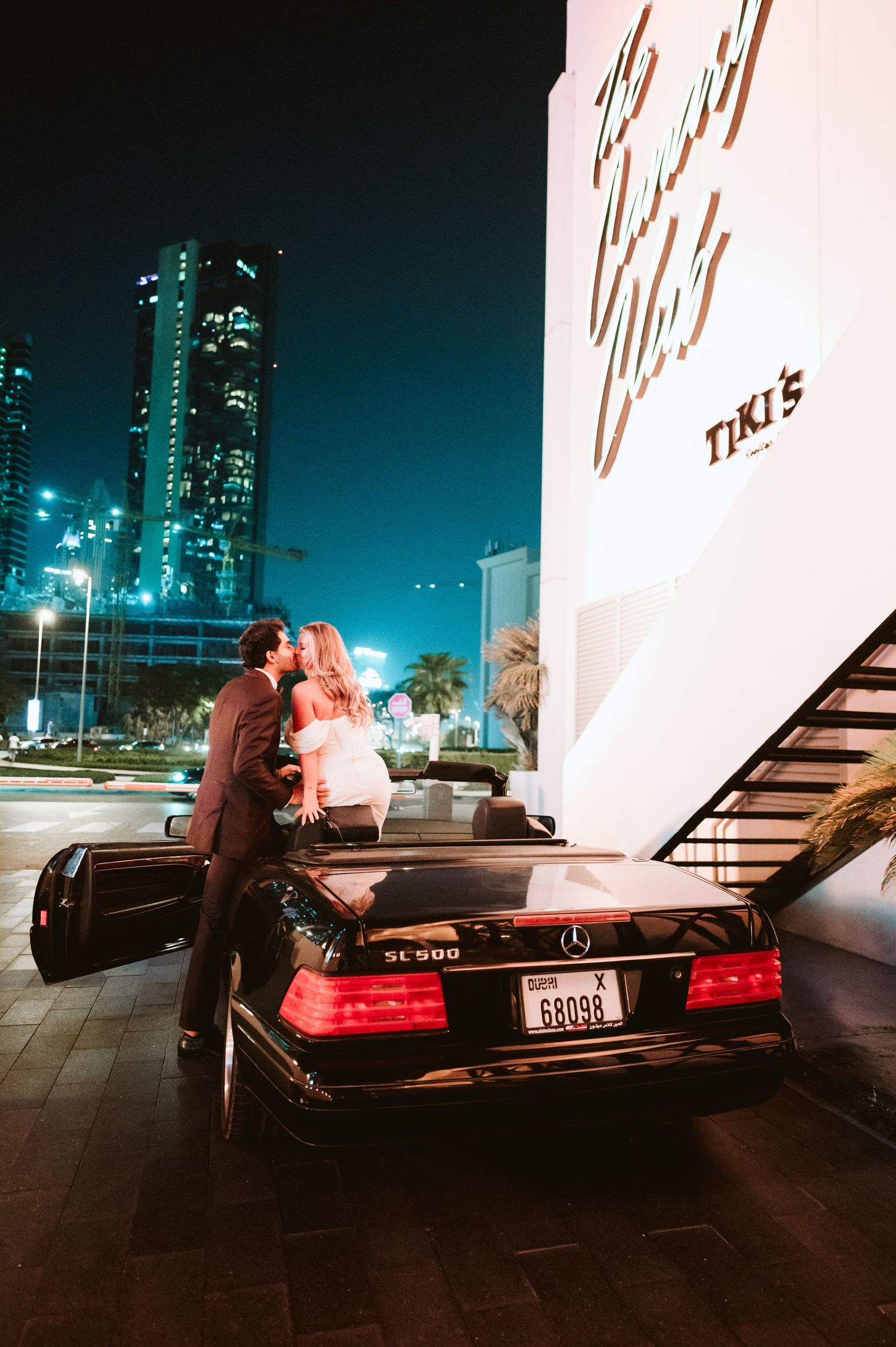 Nighttime scene with a Mercedes-Benz car against illuminated city buildings.