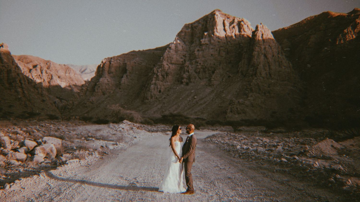 Panoramic desert wedding scene with dramatic mountain backdrop and warm lighting.