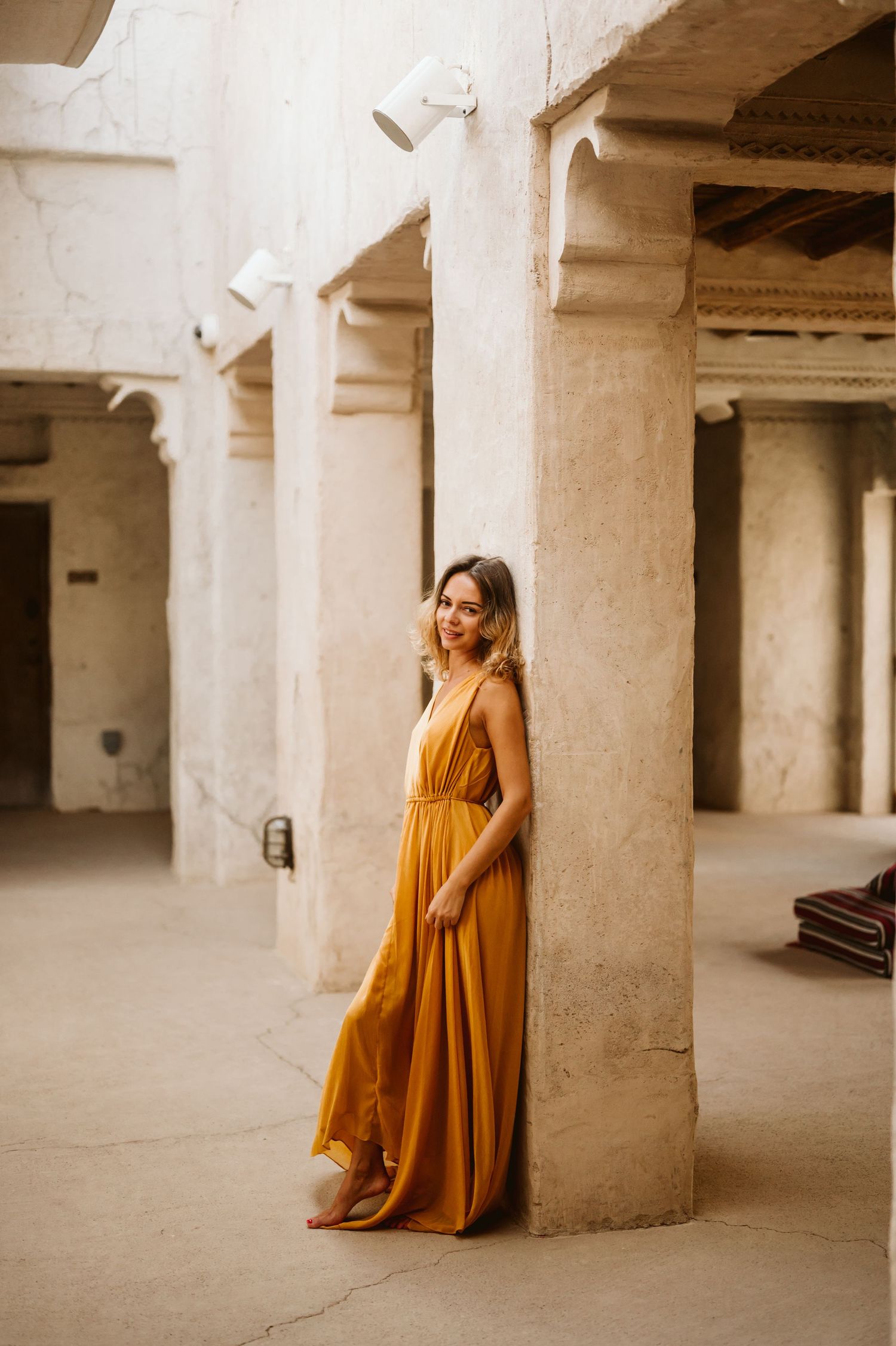 Person in flowing mustard yellow dress poses elegantly among concrete pillars.