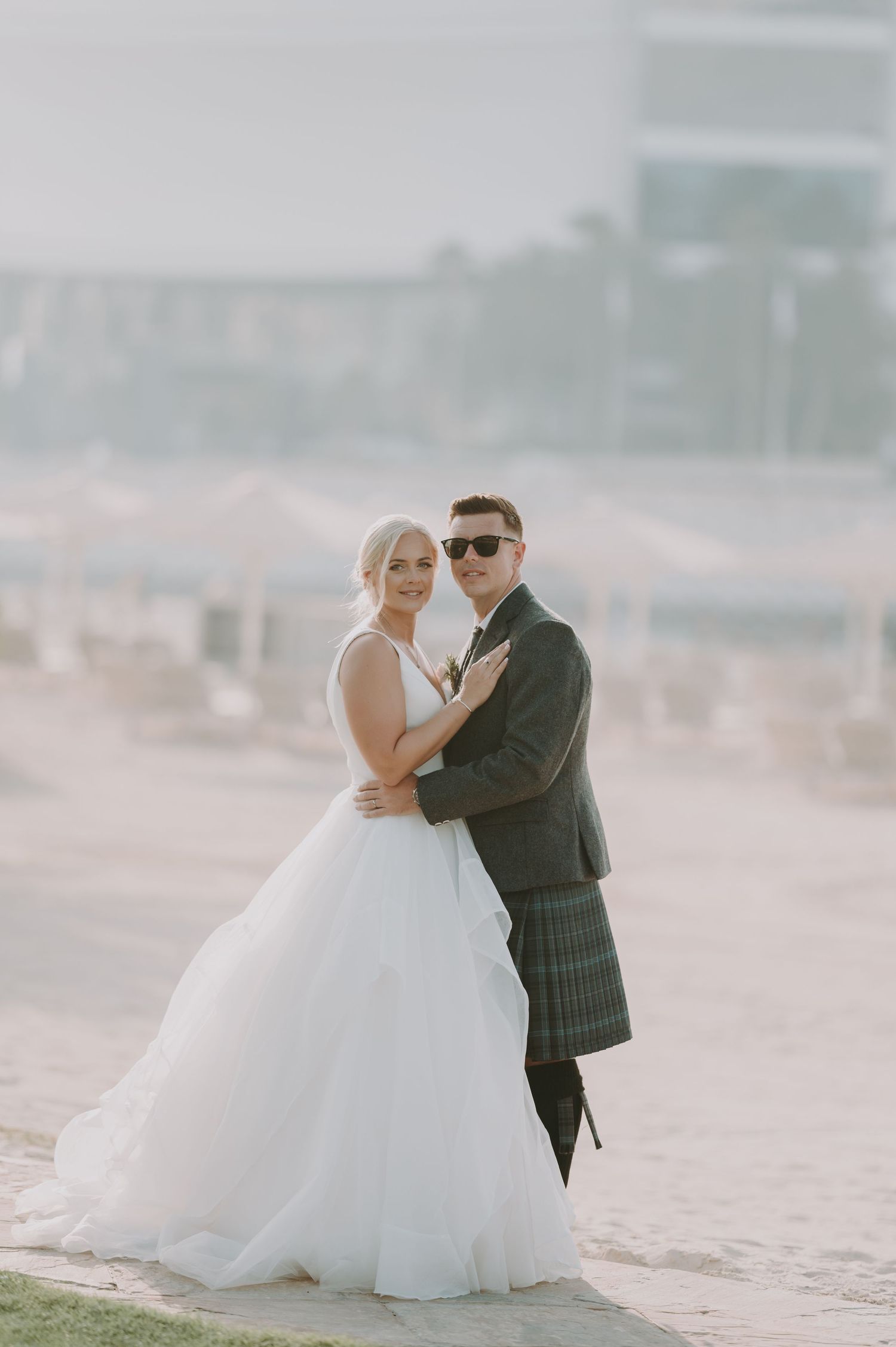A couple shares an intimate moment on a misty beach, with the bride wearing a flowing white ballgown.