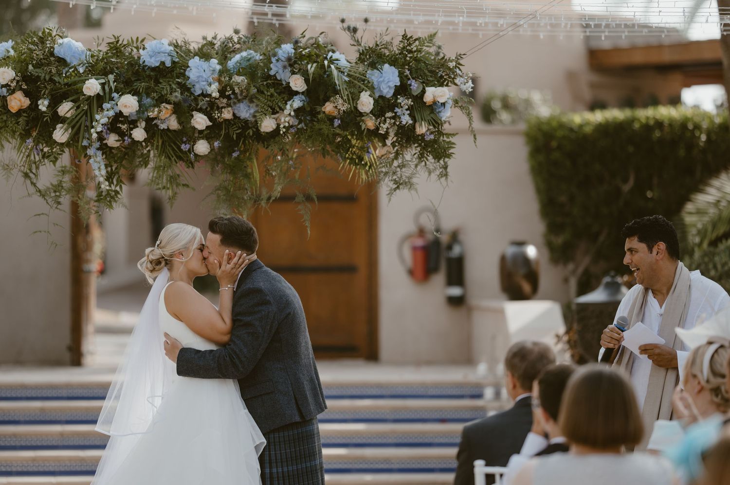 Wedding ceremony setup with white floral arrangements and wooden chairs in an outdoor venue.