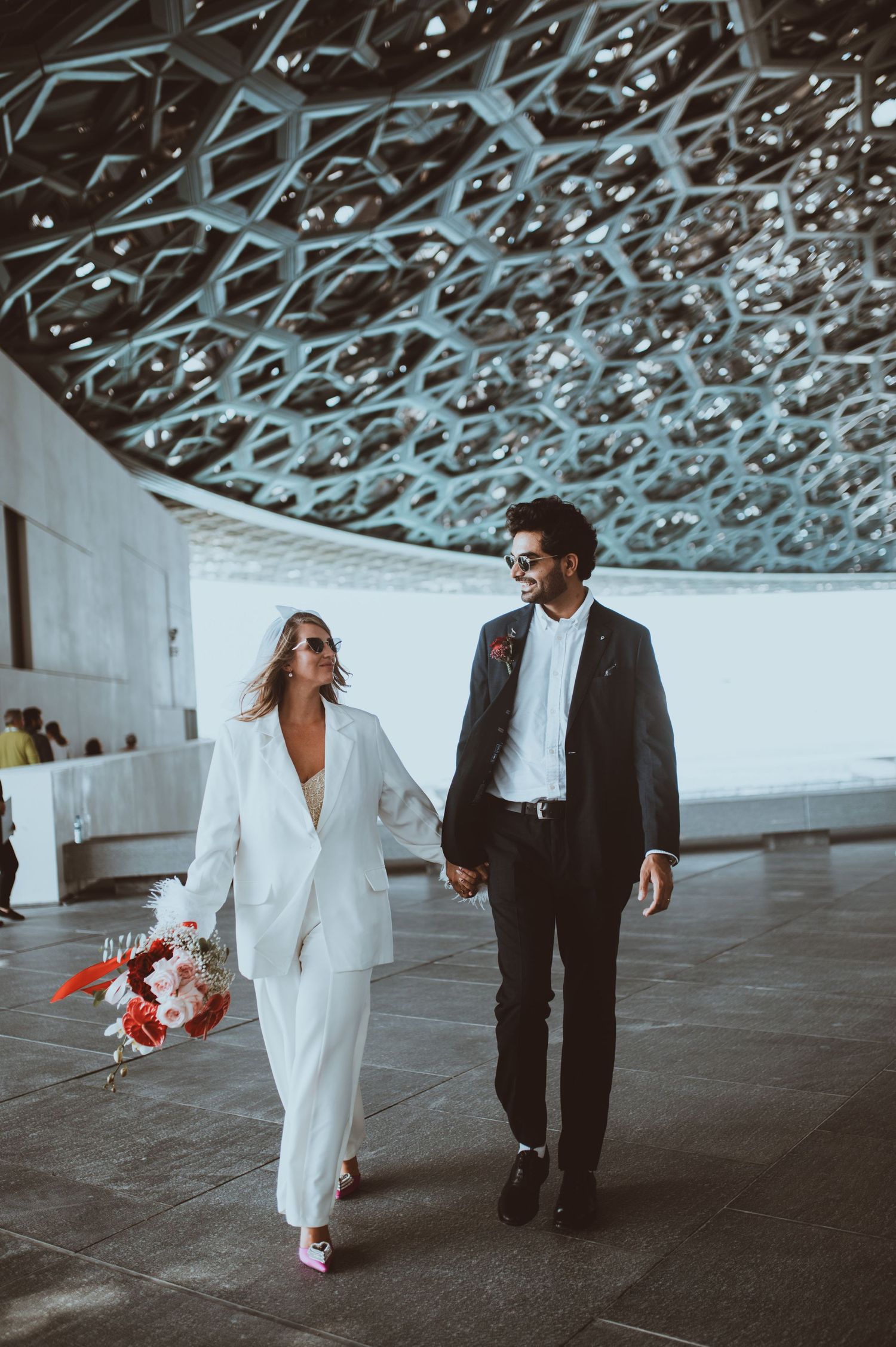 A couple walking together under a decorative ceiling, bride in white and groom in black suit.