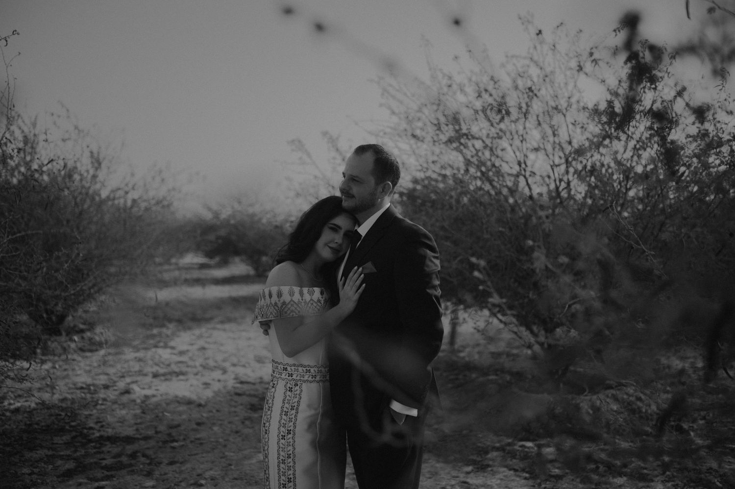 Black and white portrait of a couple embracing in a desert setting.