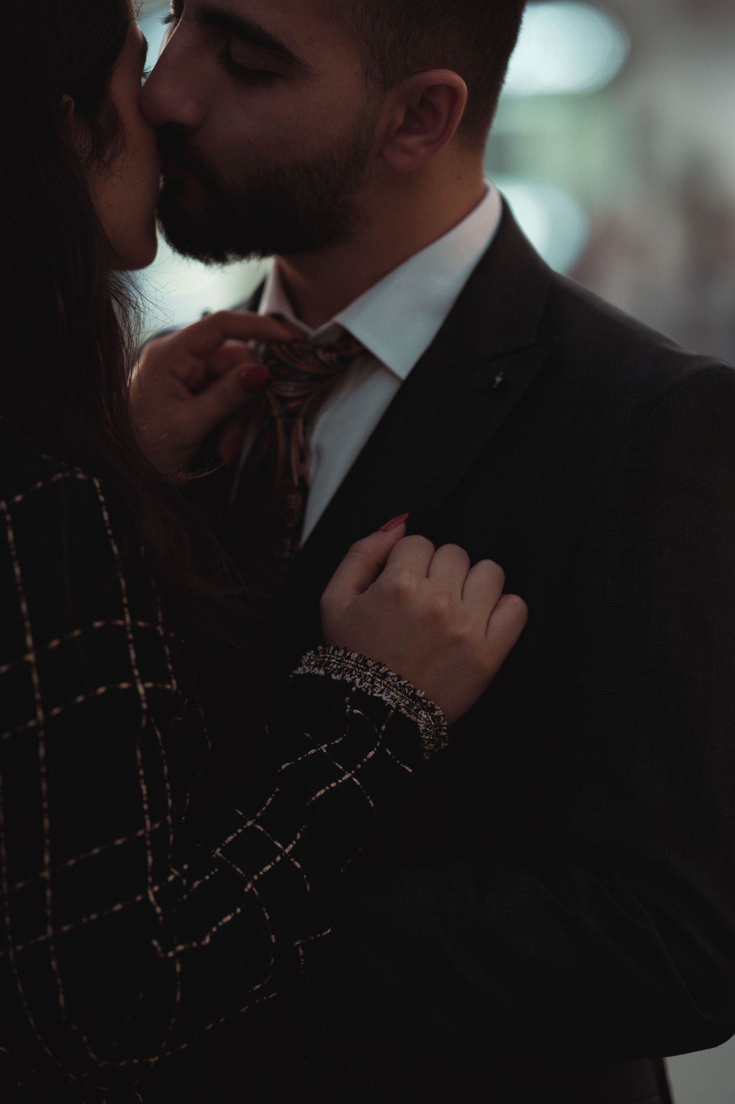 Intimate low-light portrait of couple in formal attire with dramatic shadows.