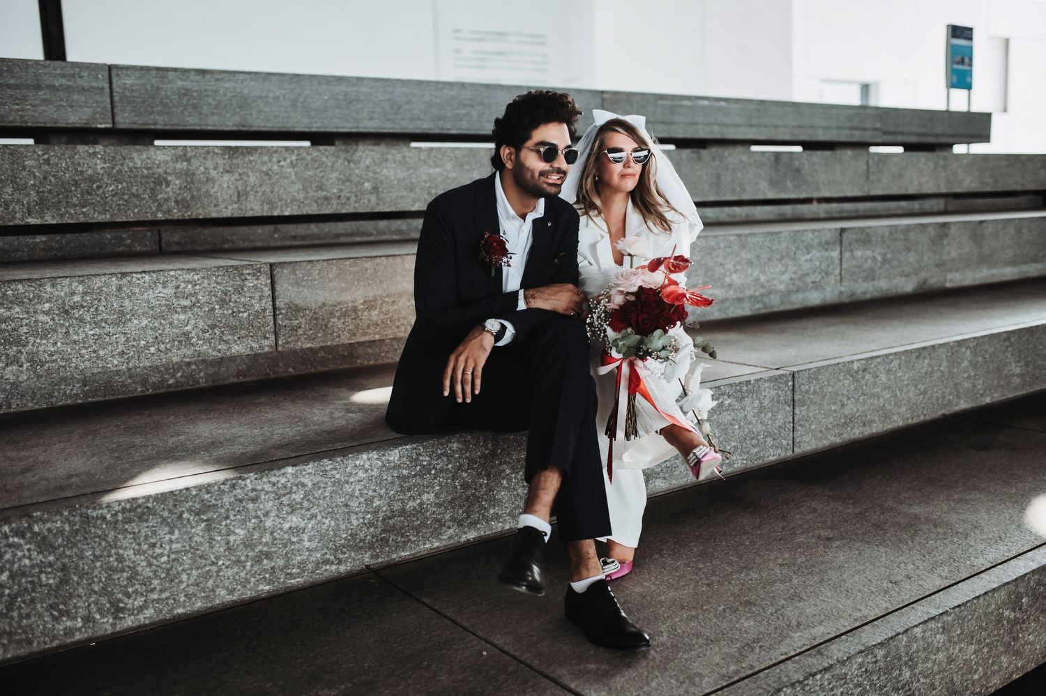 Candid wedding moments captured on modern architectural steps in moody lighting.