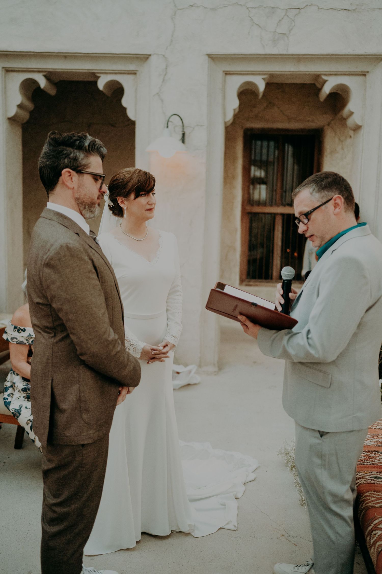 Wedding ceremony participants reading documents against a white marble wall backdrop.