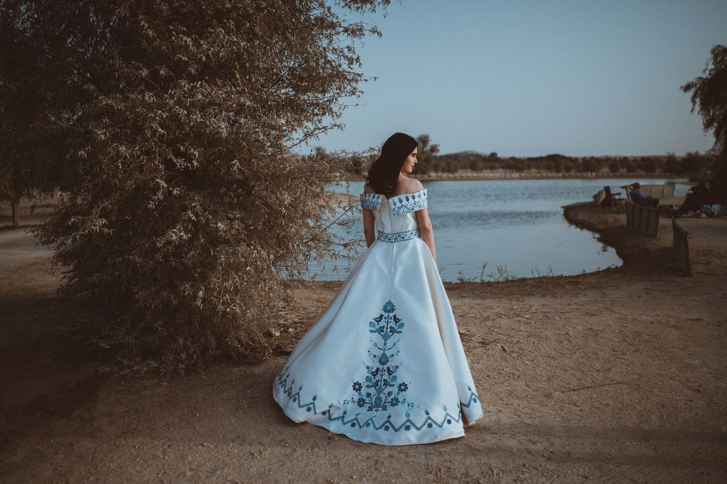 A waterfront wedding photo shows a bride in a blue-detailed white gown against a natural backdrop.