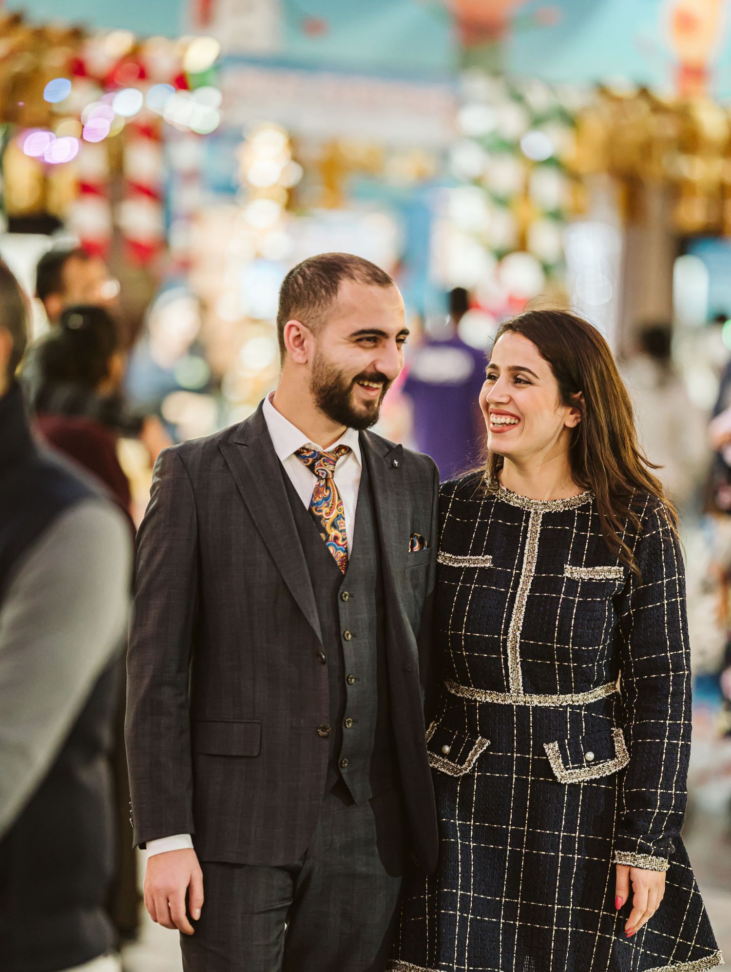 A couple shares a joyful moment together while wearing coordinated black and tweed outfits in a festive setting.