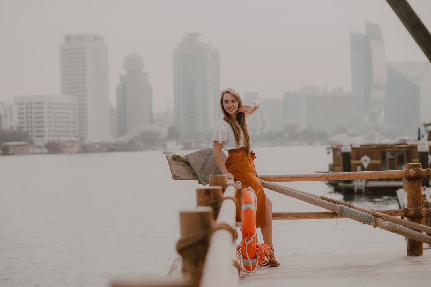 Cityscape view with person in orange dress on waterfront deck.