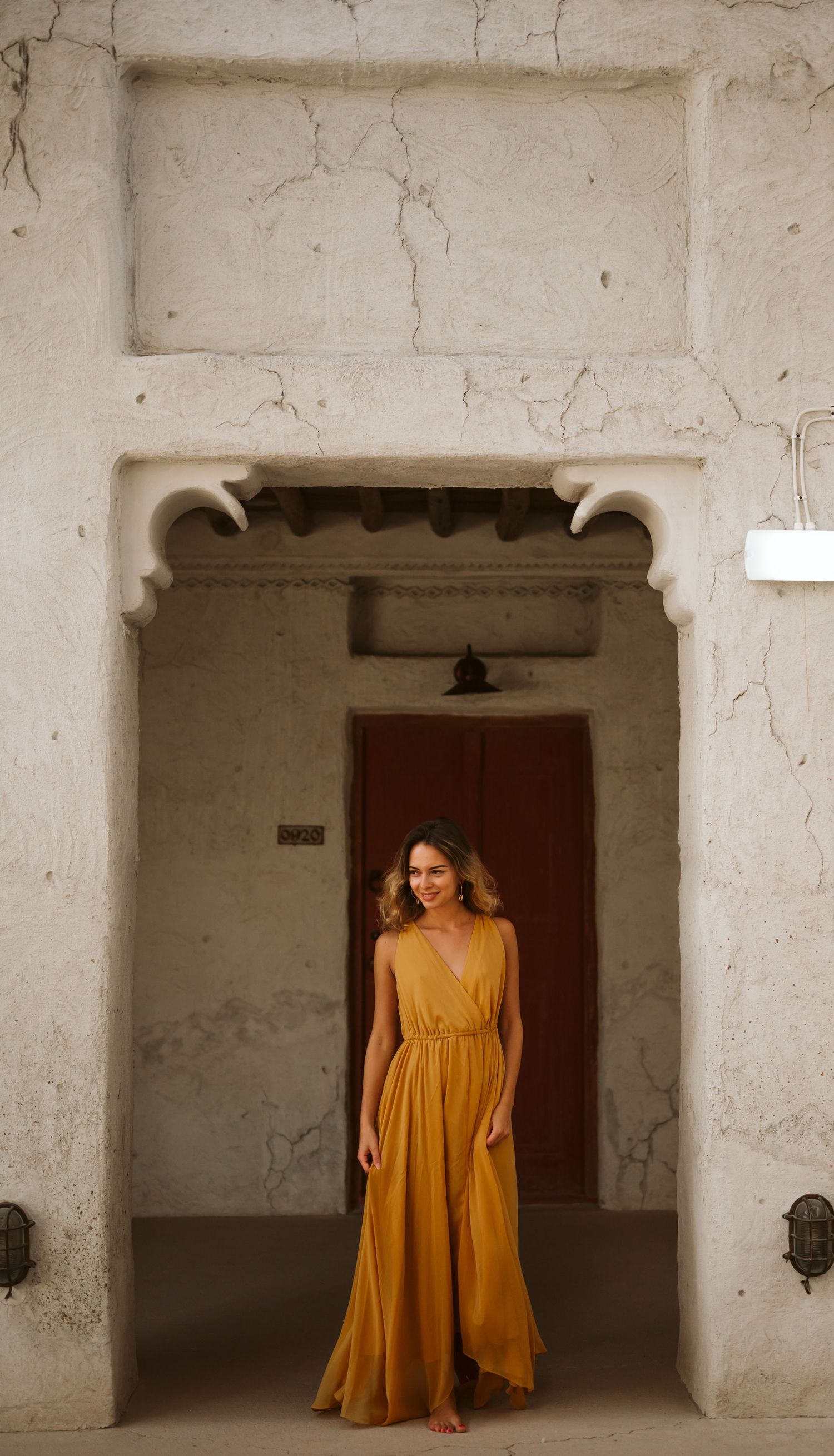 A mustard yellow dress flows elegantly against white stone archways in an architectural setting.