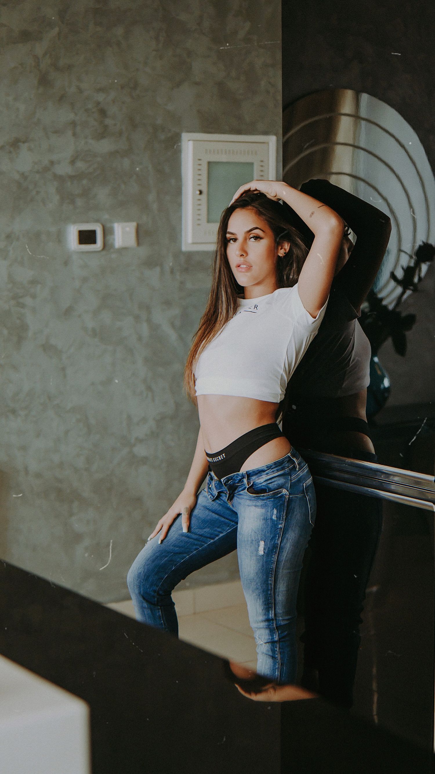 Lifestyle portrait of a woman in casual attire posing against an industrial wall.