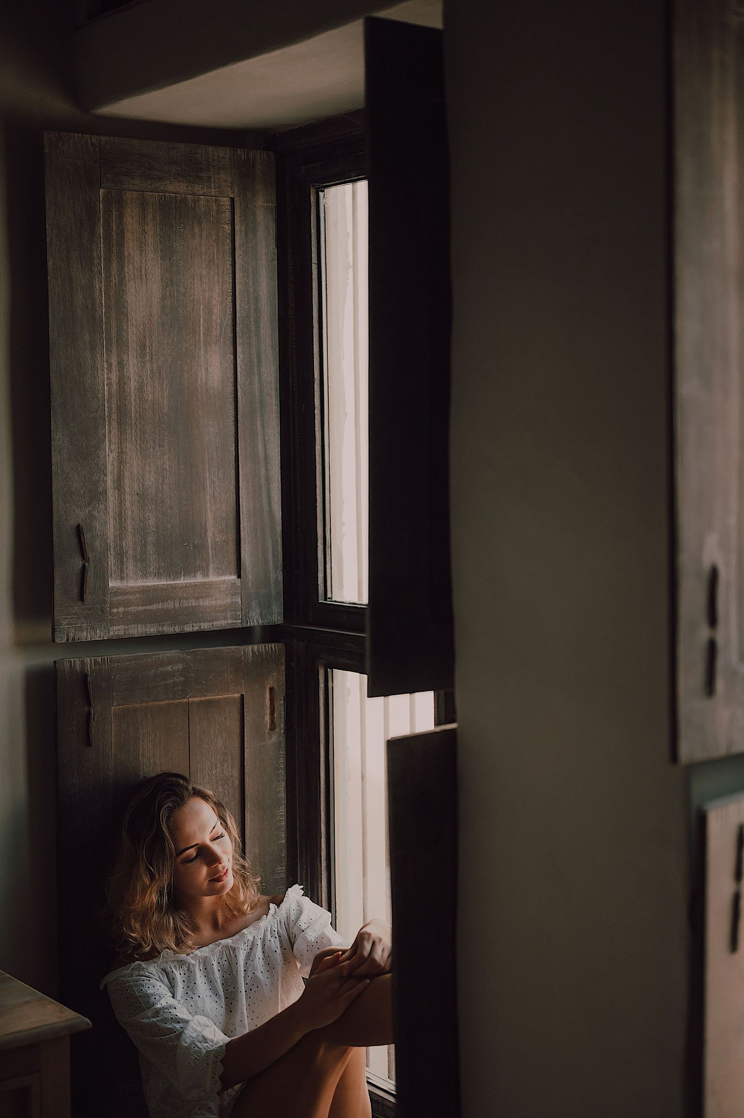 Atmospheric portrait by a window with moody natural lighting.