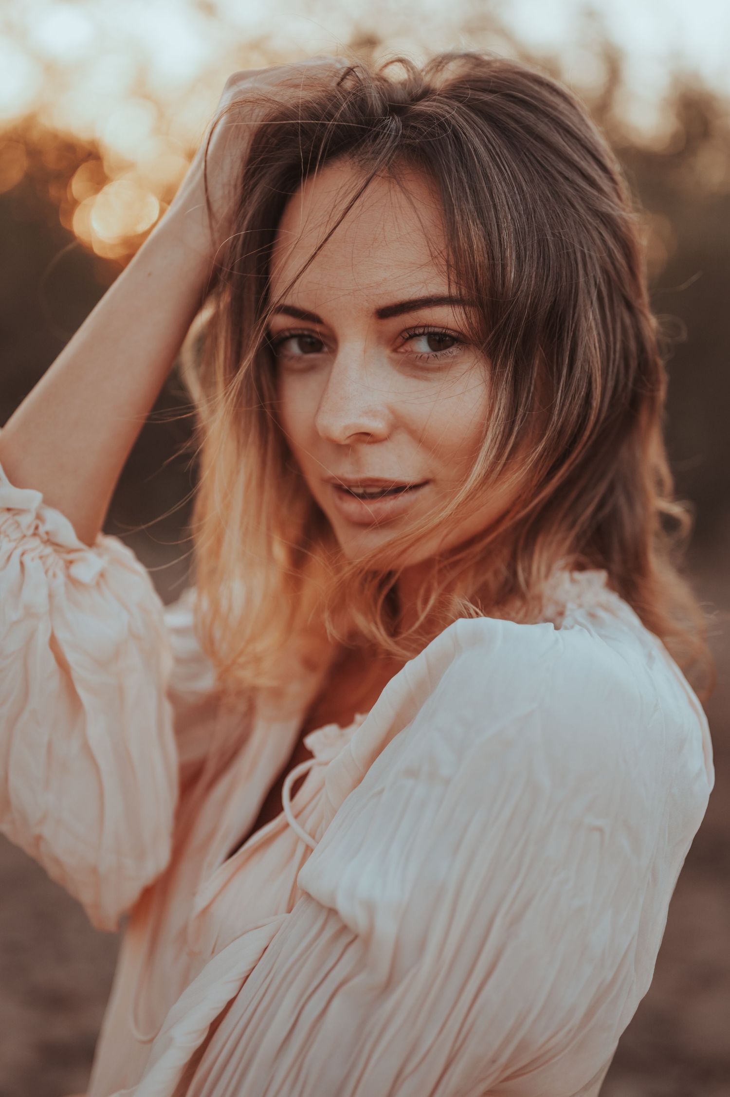 Warm sunset portrait with soft bokeh lighting and flowing white blouse.