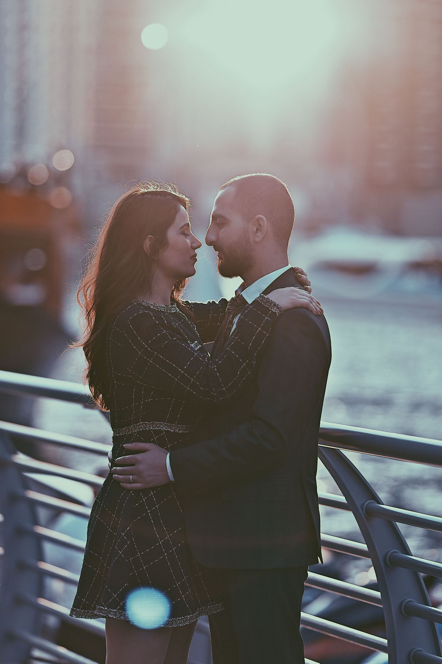 Romantic couple embracing on a waterfront with soft sunset lighting.