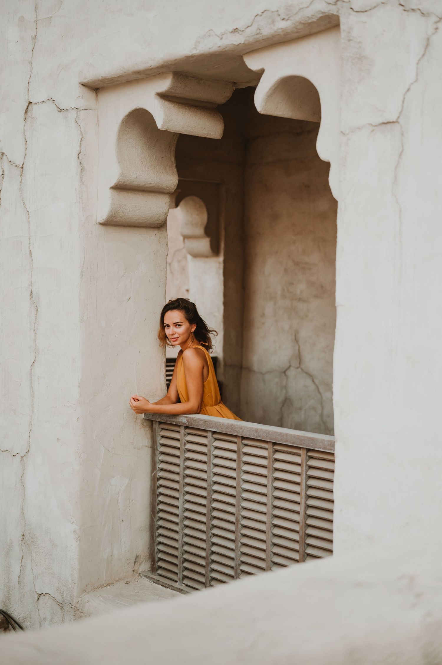 A mustard-colored dress contrasts against white architectural details and geometric patterns.