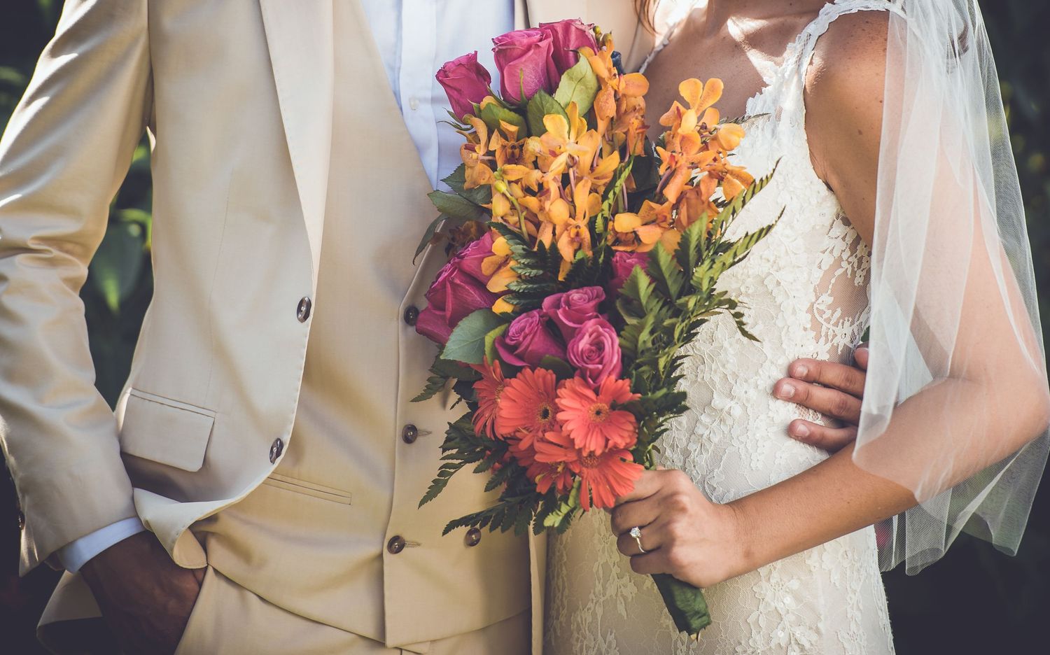 Close-up of newlyweds holding a vibrant wedding bouquet with pink and orange flowers.