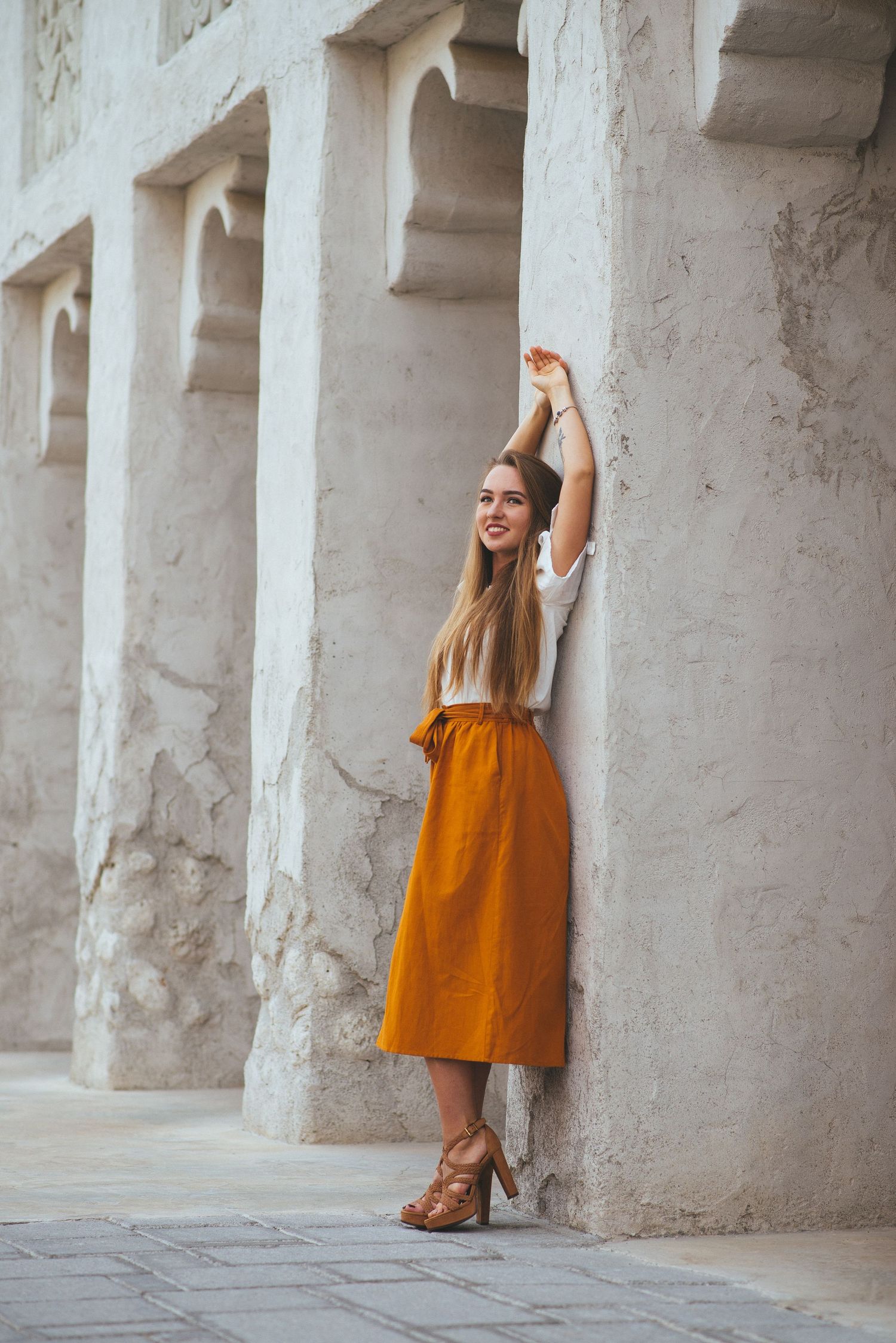 Person in orange skirt posing against white stone columns.