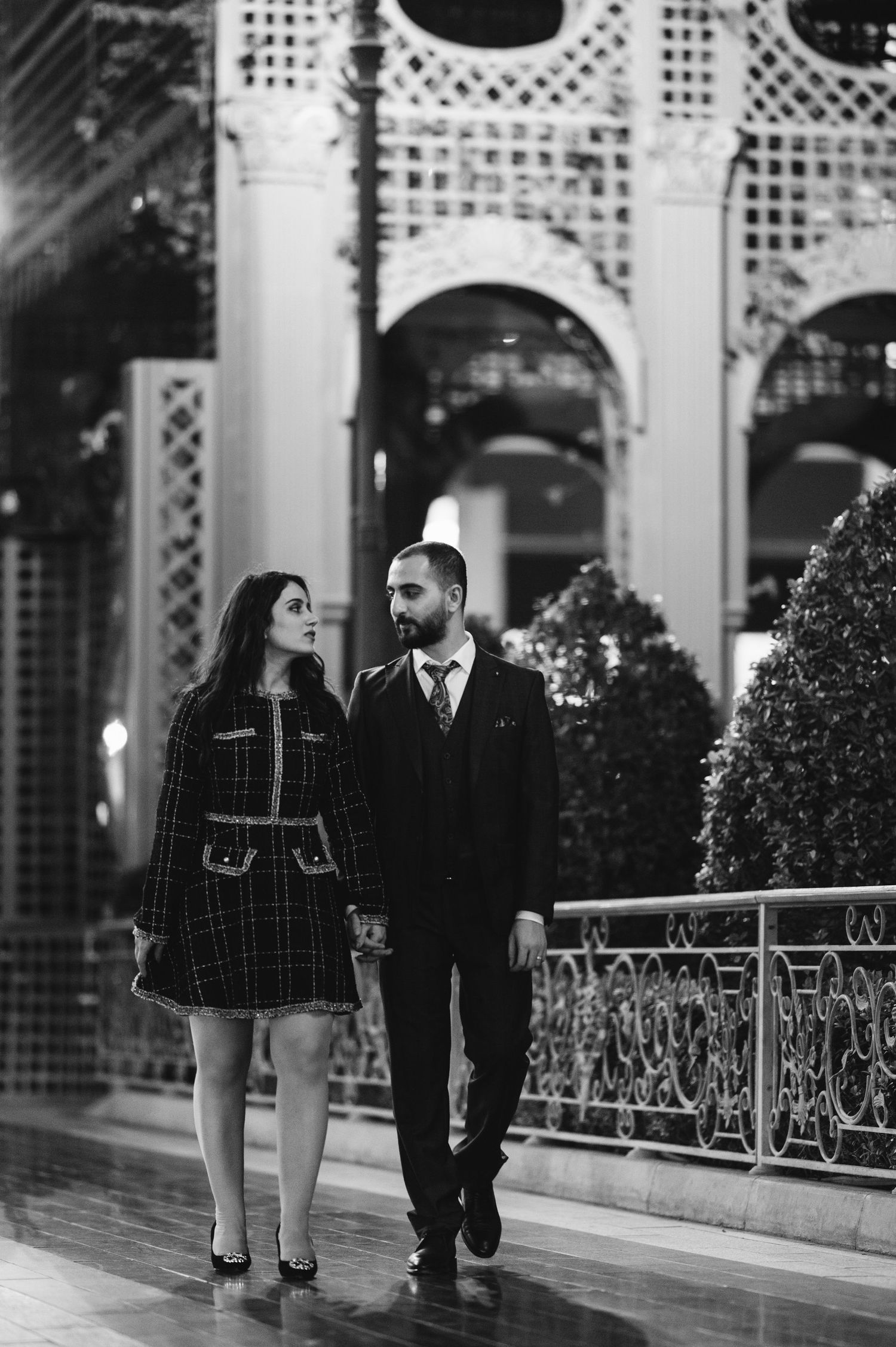 Elegant couple walking together along a decorative white lattice walkway.