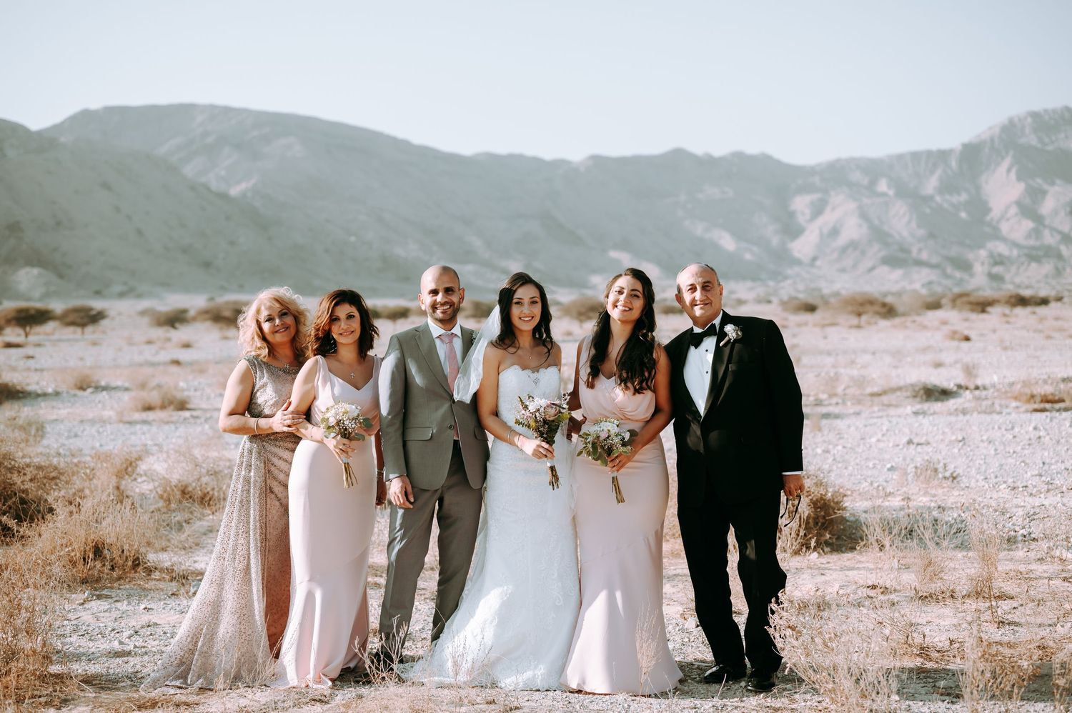 Wedding party poses together in desert landscape with mountains in background.