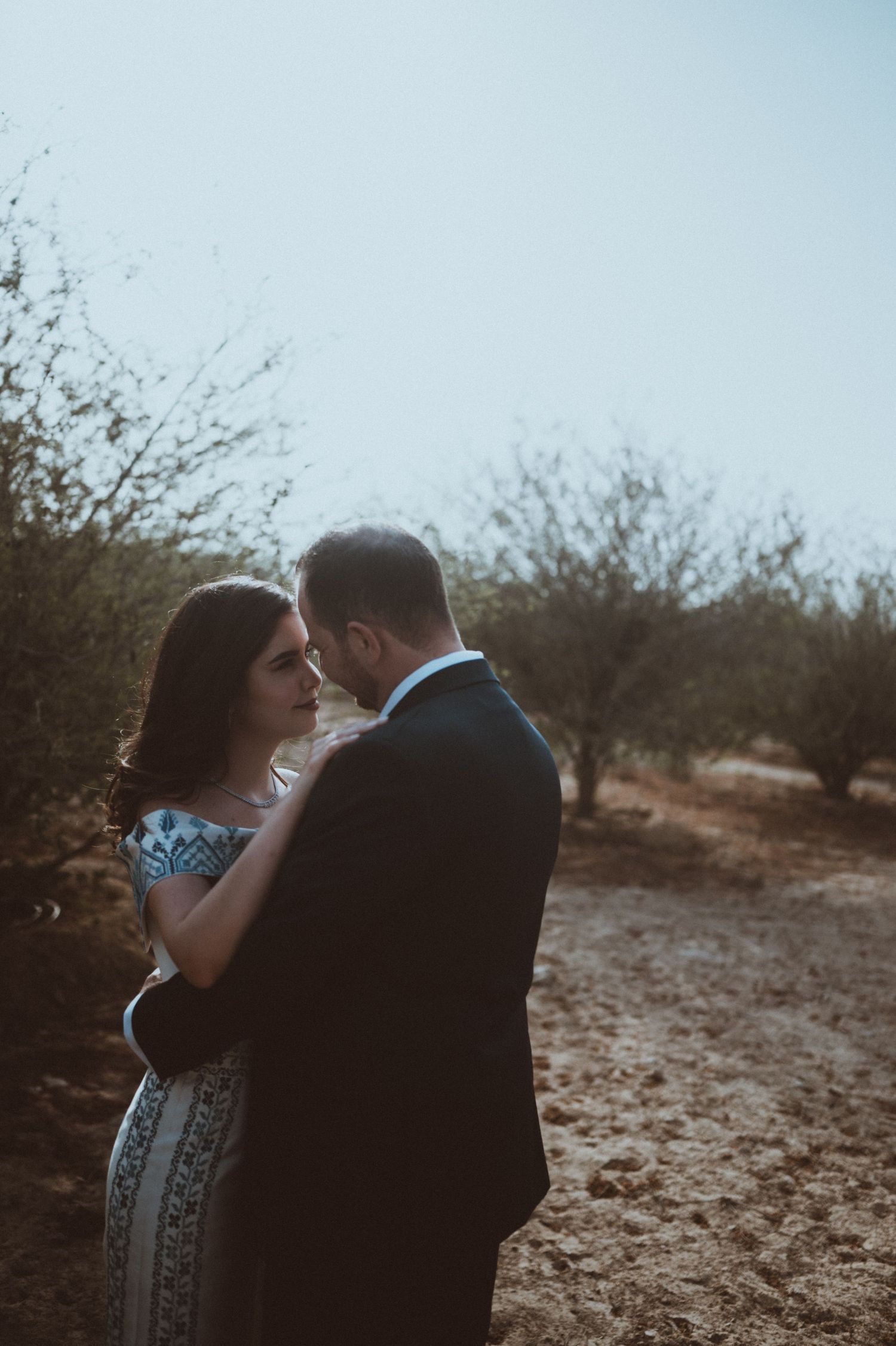 Intimate couple's portrait in muted tones against desert brush background.