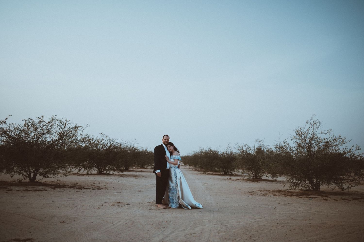 A panoramic view of a desert landscape with scattered trees and a couple in the distance.