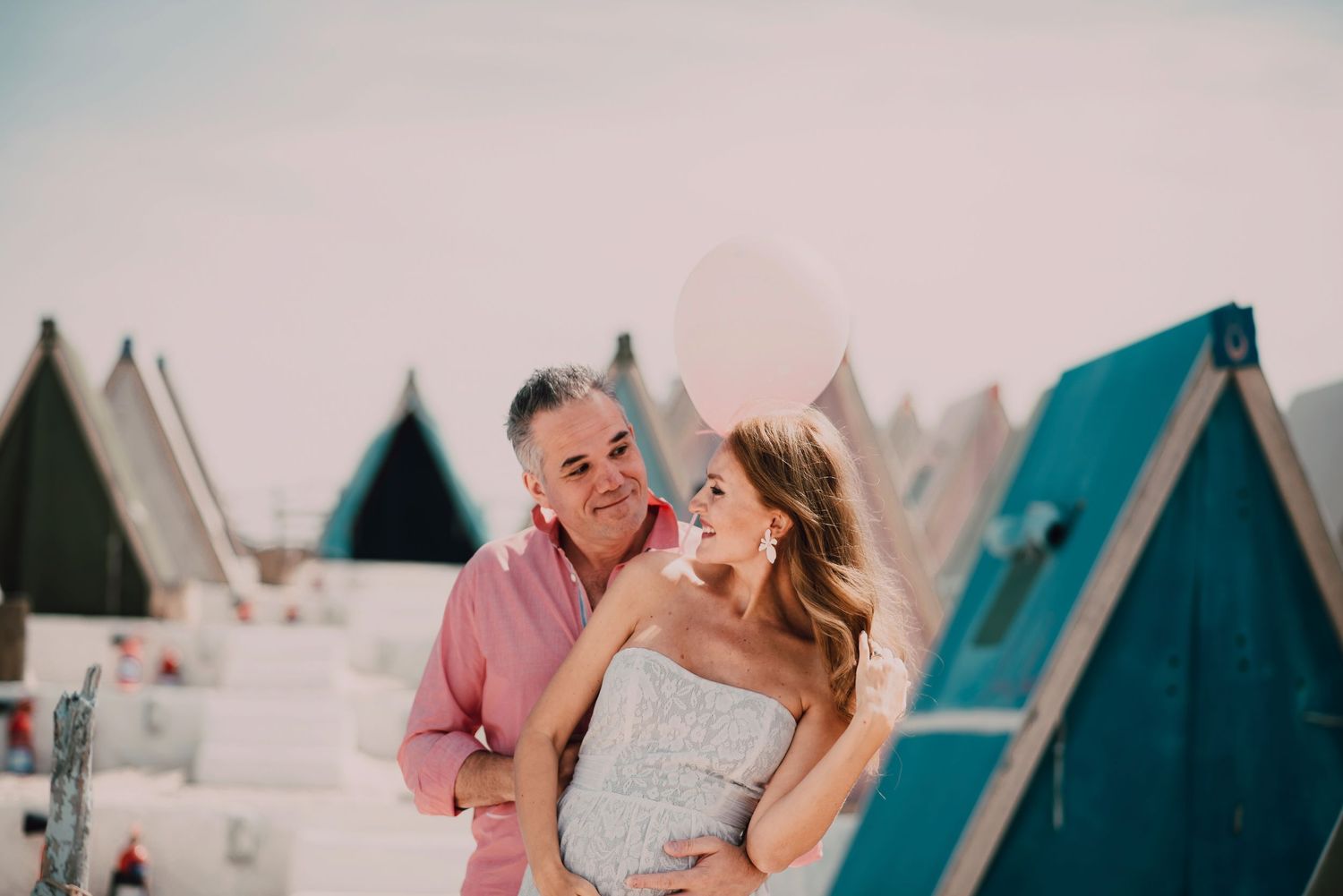 Romantic beachside photo session with couple in white and pink outfits against ocean backdrop.