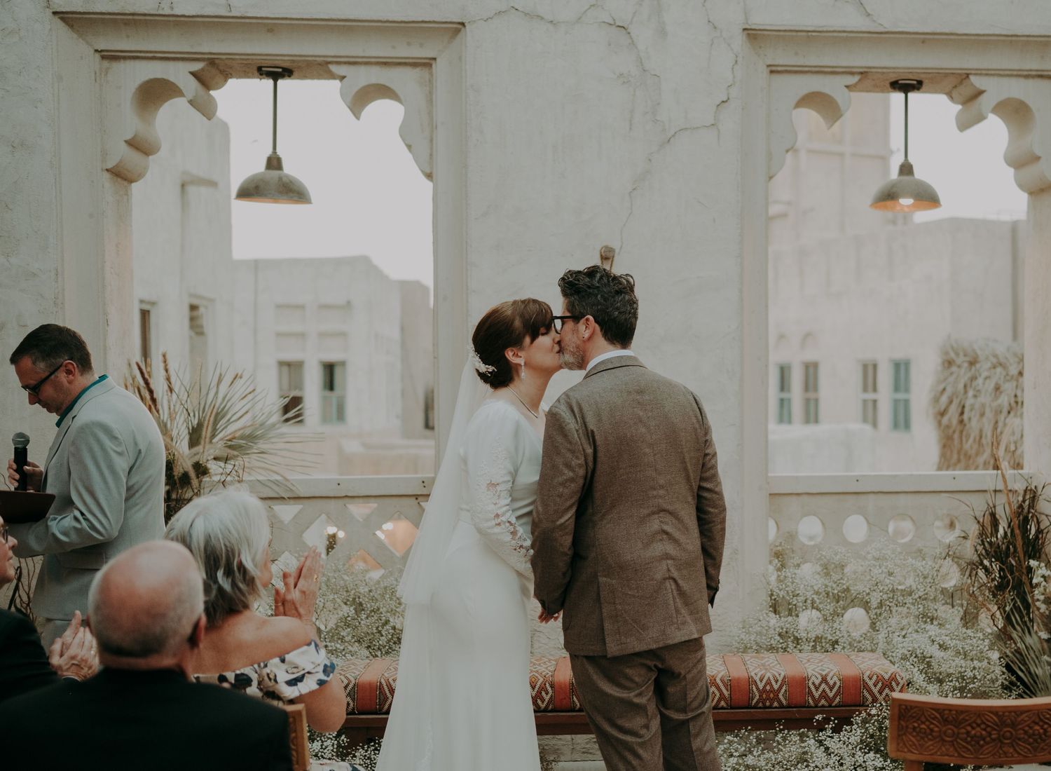 Wedding ceremony guests gather in a light-filled room with white walls and elegant architectural details.