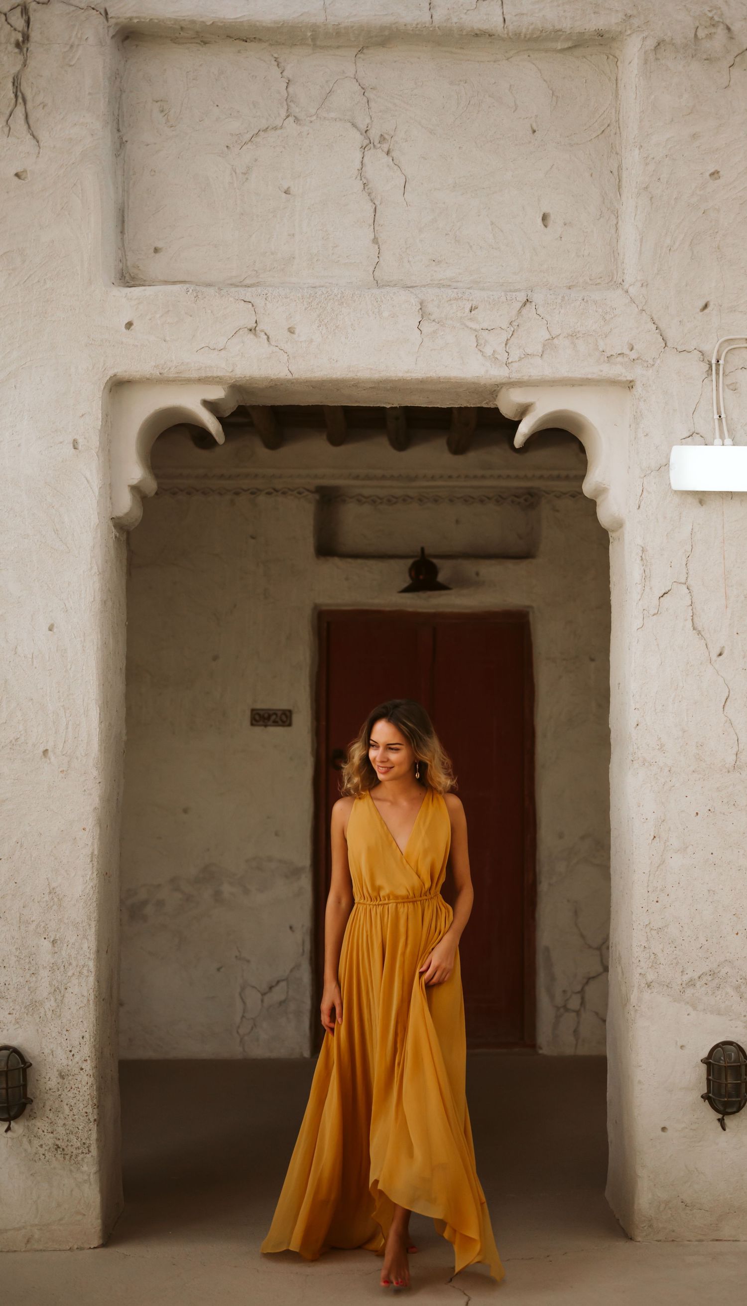 A flowing marigold dress creates movement and drama against textured white stone walls and arches.