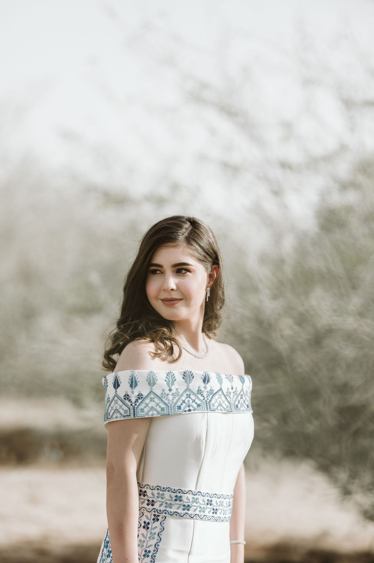 Elegant off-shoulder white dress with blue embroidered details photographed in soft natural lighting.