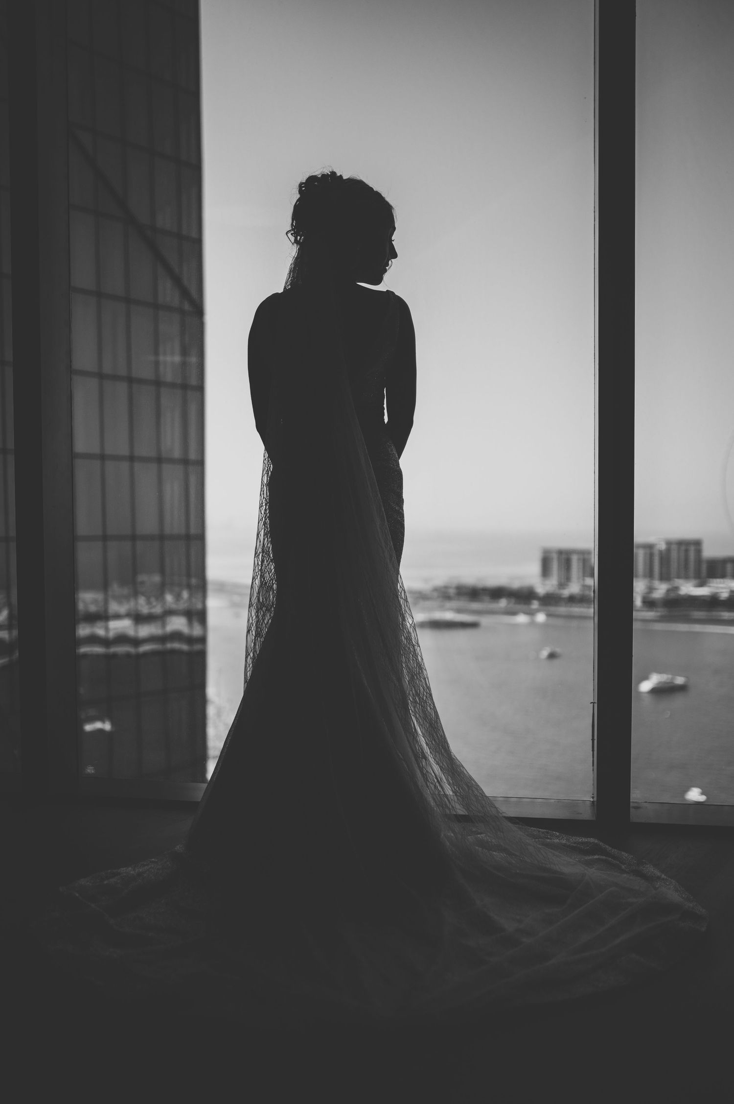 Dramatic silhouette of figures against window with ocean view in black and white.