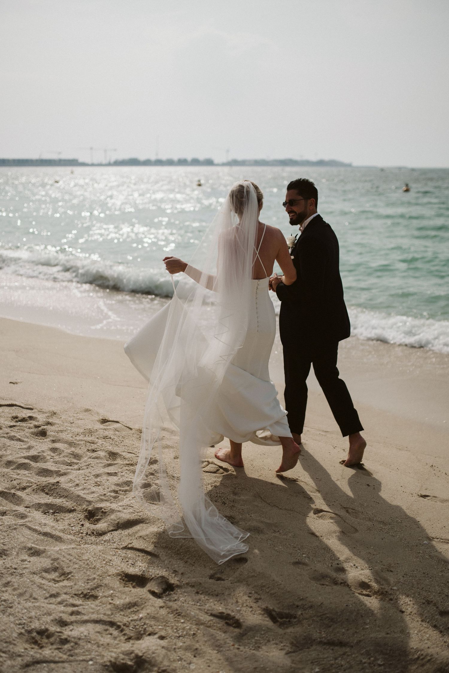 Newlyweds share a joyful moment dancing together on a sandy beach.