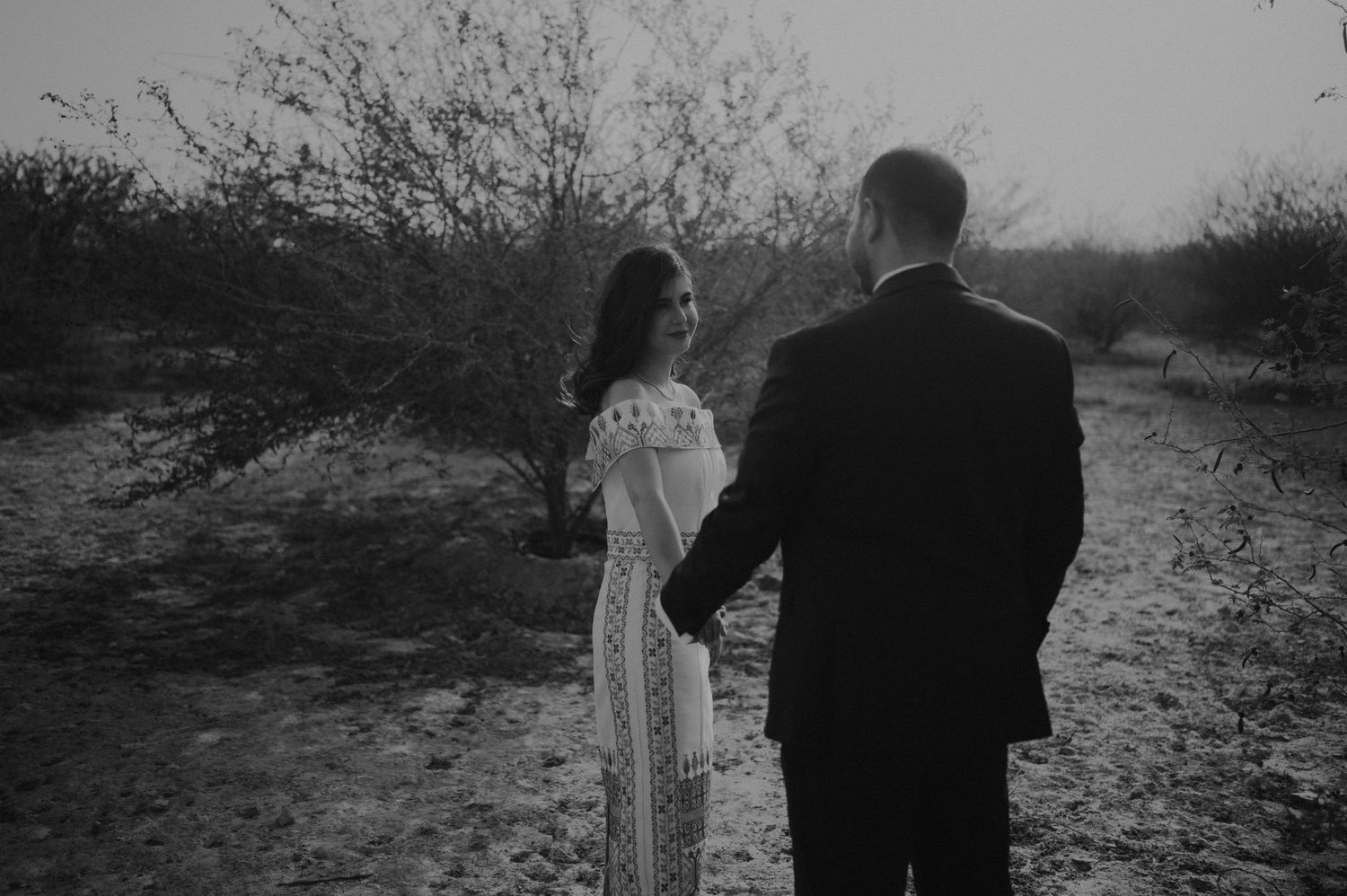 Monochrome image of a couple walking through desert brush during sunset.