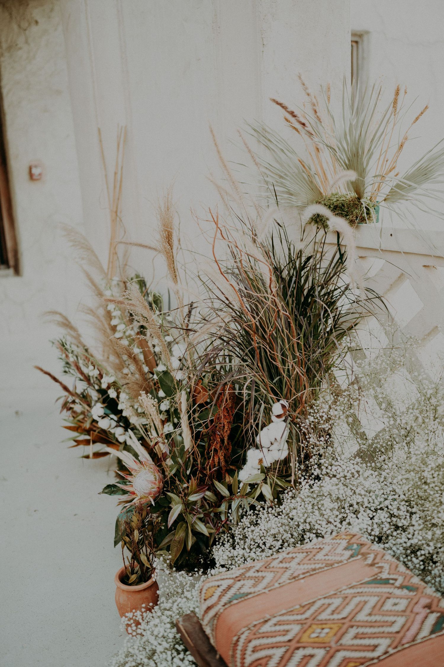 Dried floral arrangements with pampas grass and baby's breath accent an orange cushioned bench.