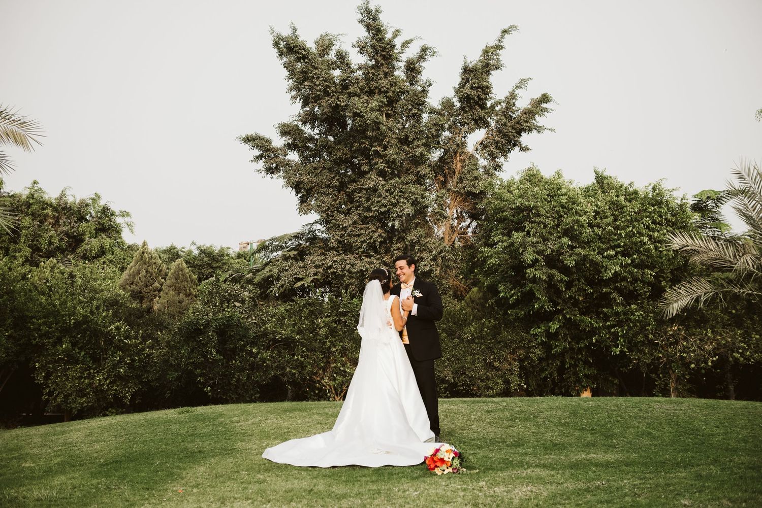 Wedding couple poses in scenic garden setting surrounded by lush greenery.