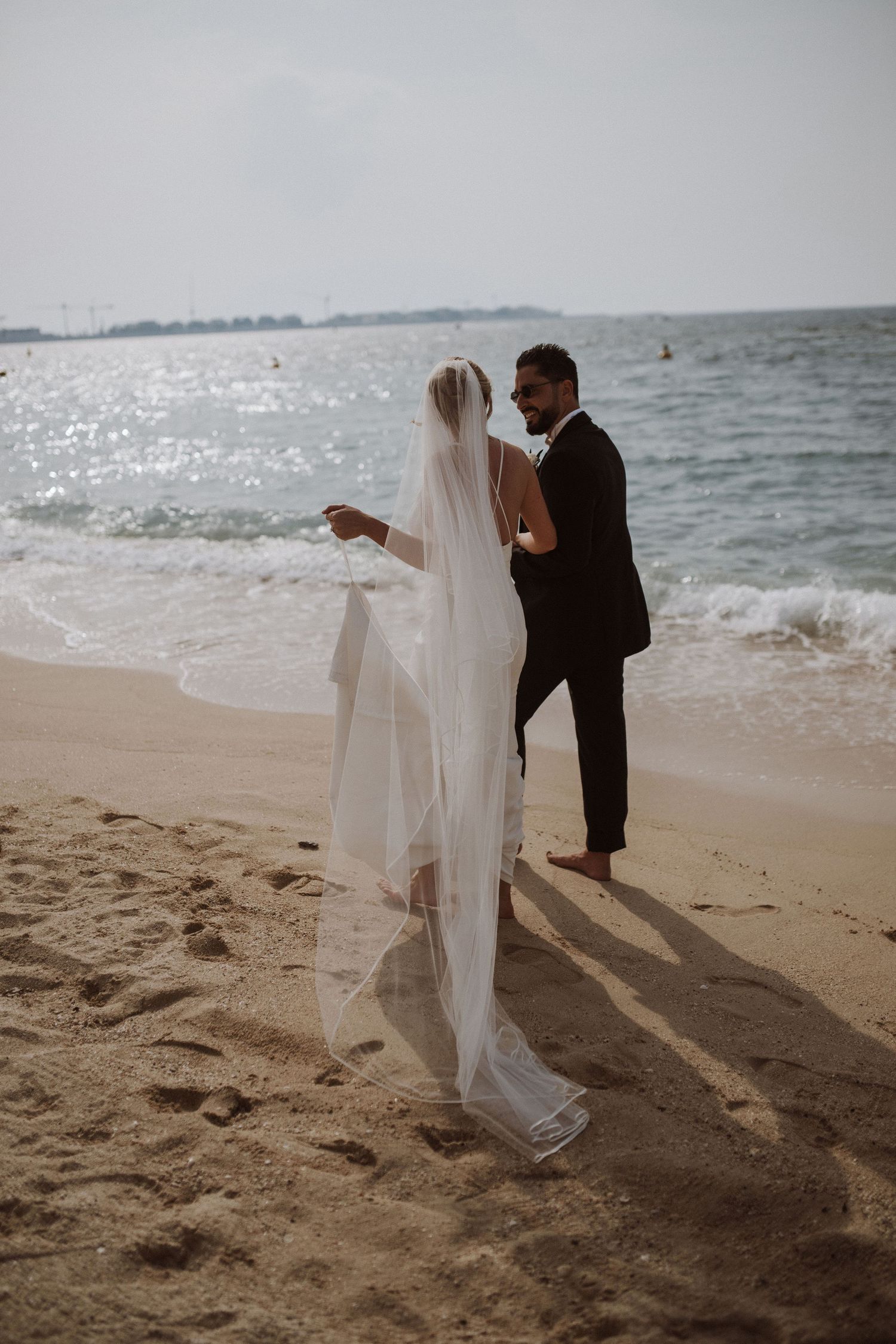 A couple dances playfully on the beach with the bride's veil flowing in the wind.