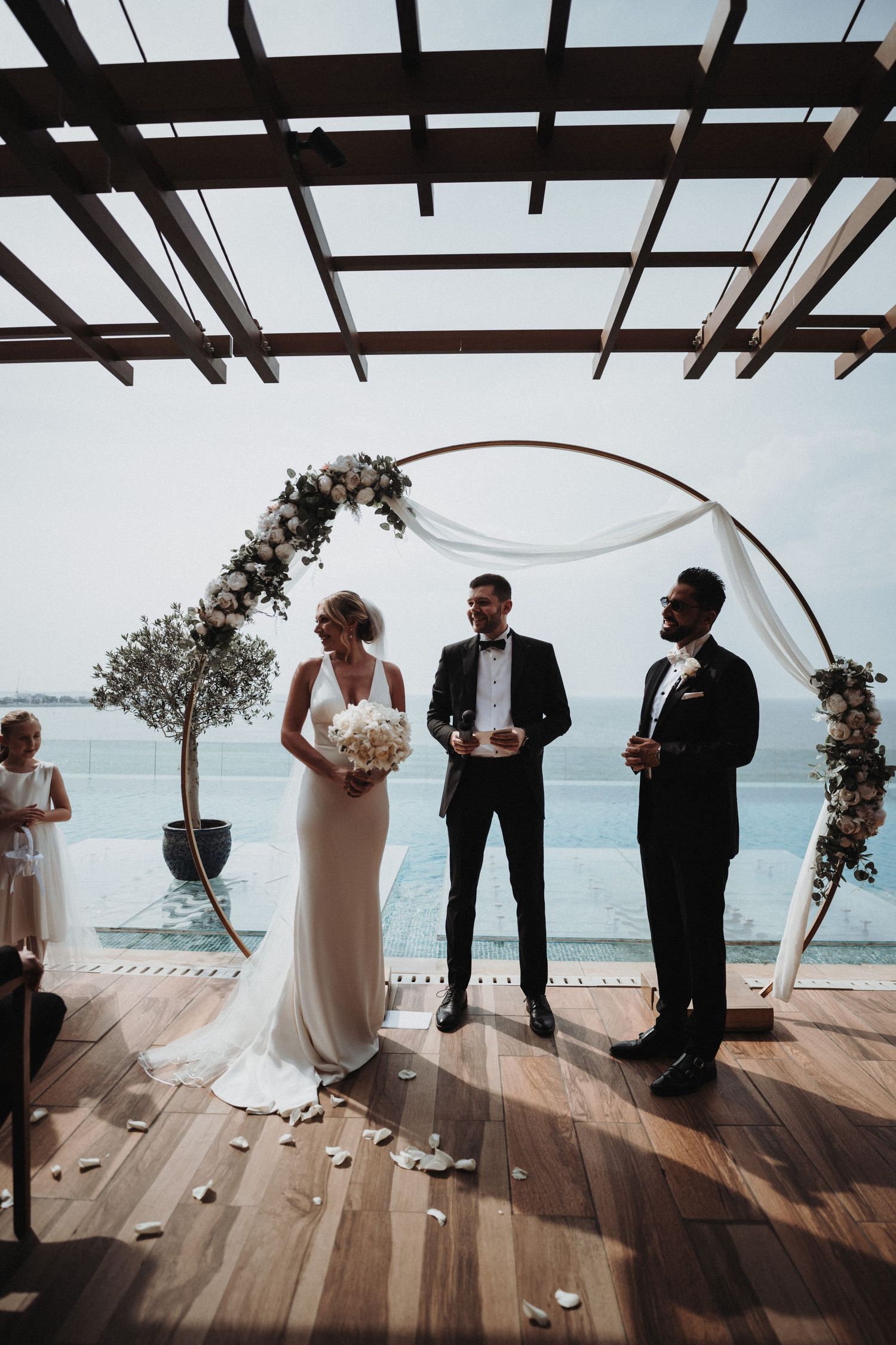 A beachfront wedding ceremony with an arch decorated with flowers against the blue ocean backdrop.