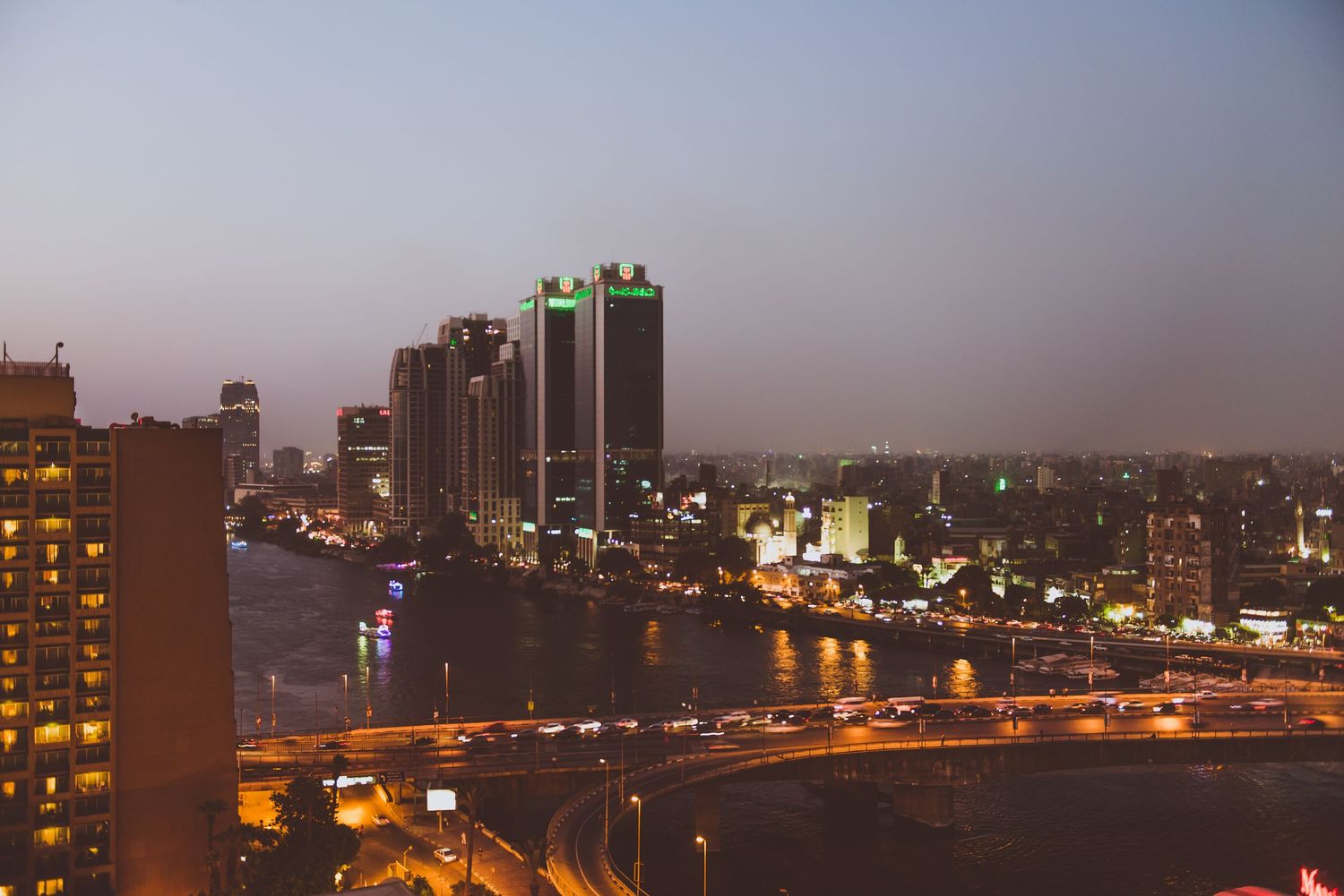 Panoramic cityscape view of an urban skyline at dusk with illuminated buildings.