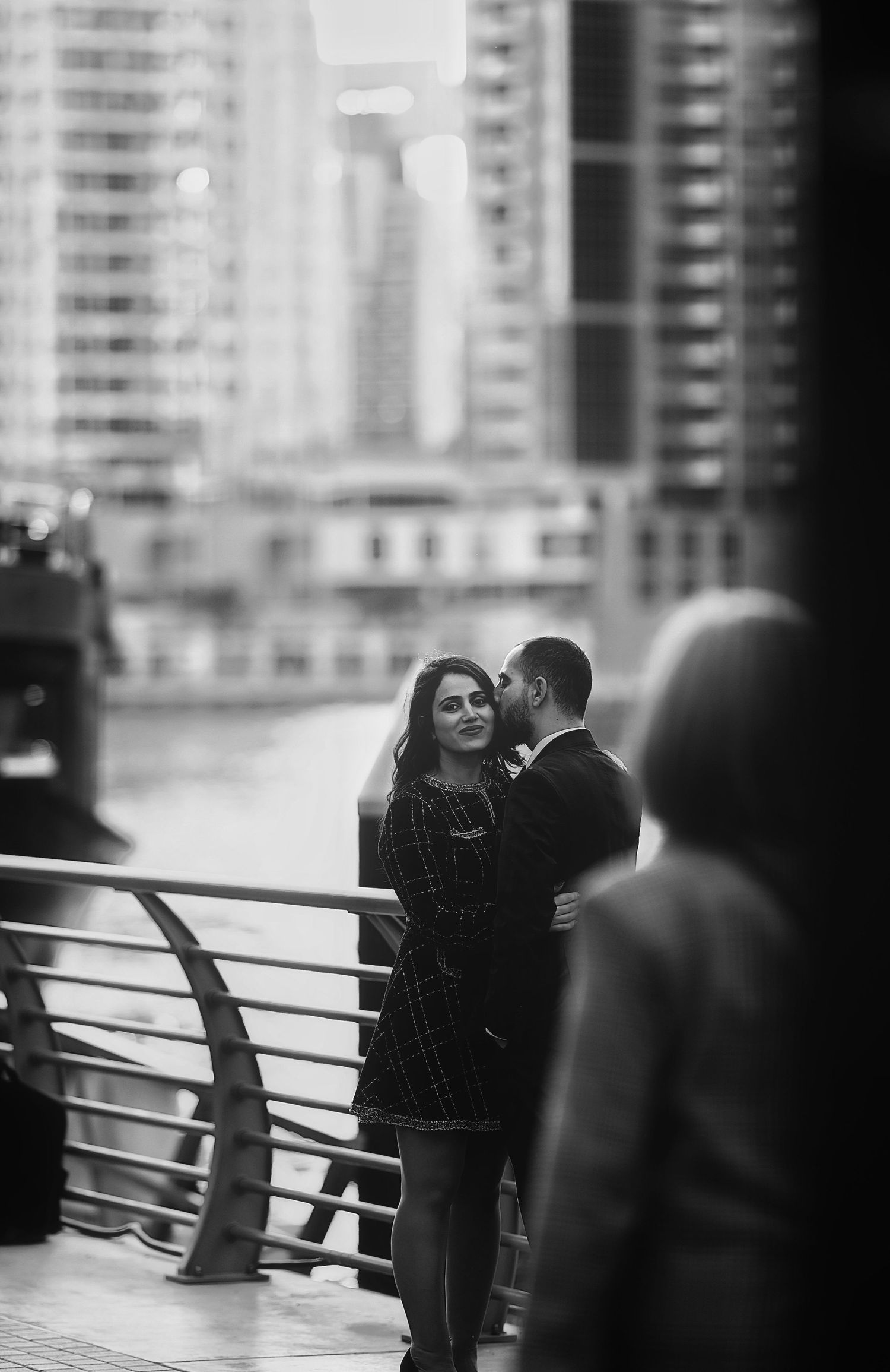 Black and white portrait of couple sharing intimate moment along city waterfront.