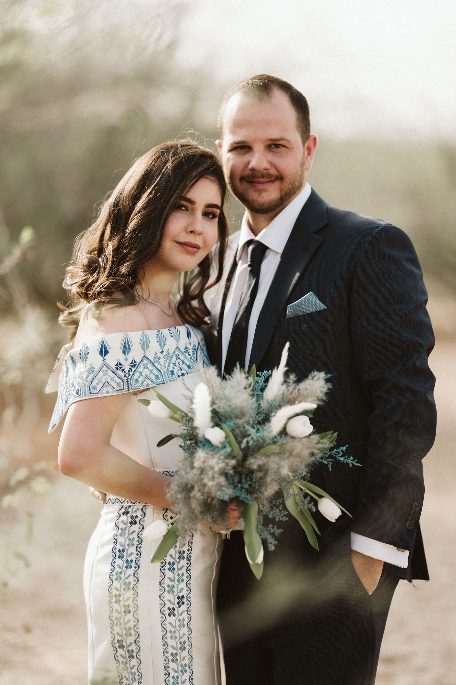 A romantic wedding photo shows a couple embracing outdoors in formal attire with a unique blue and white dress.
