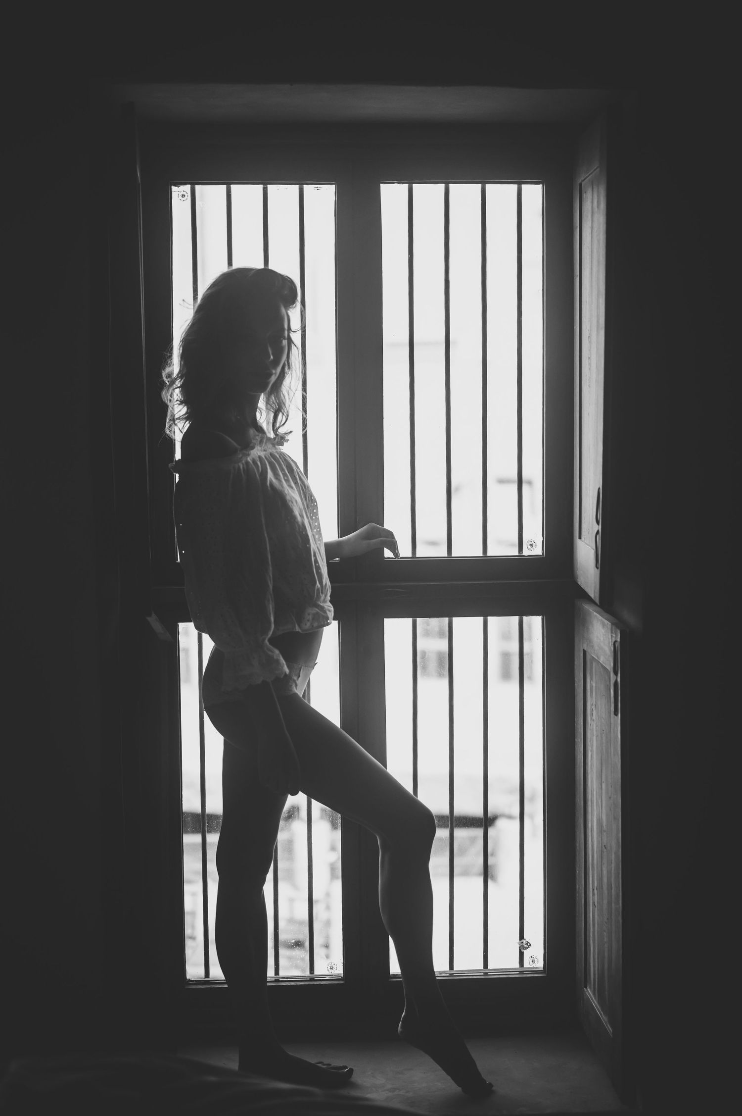 Silhouetted figure stands in dramatic lighting by a window with vertical bars creating moody atmosphere.