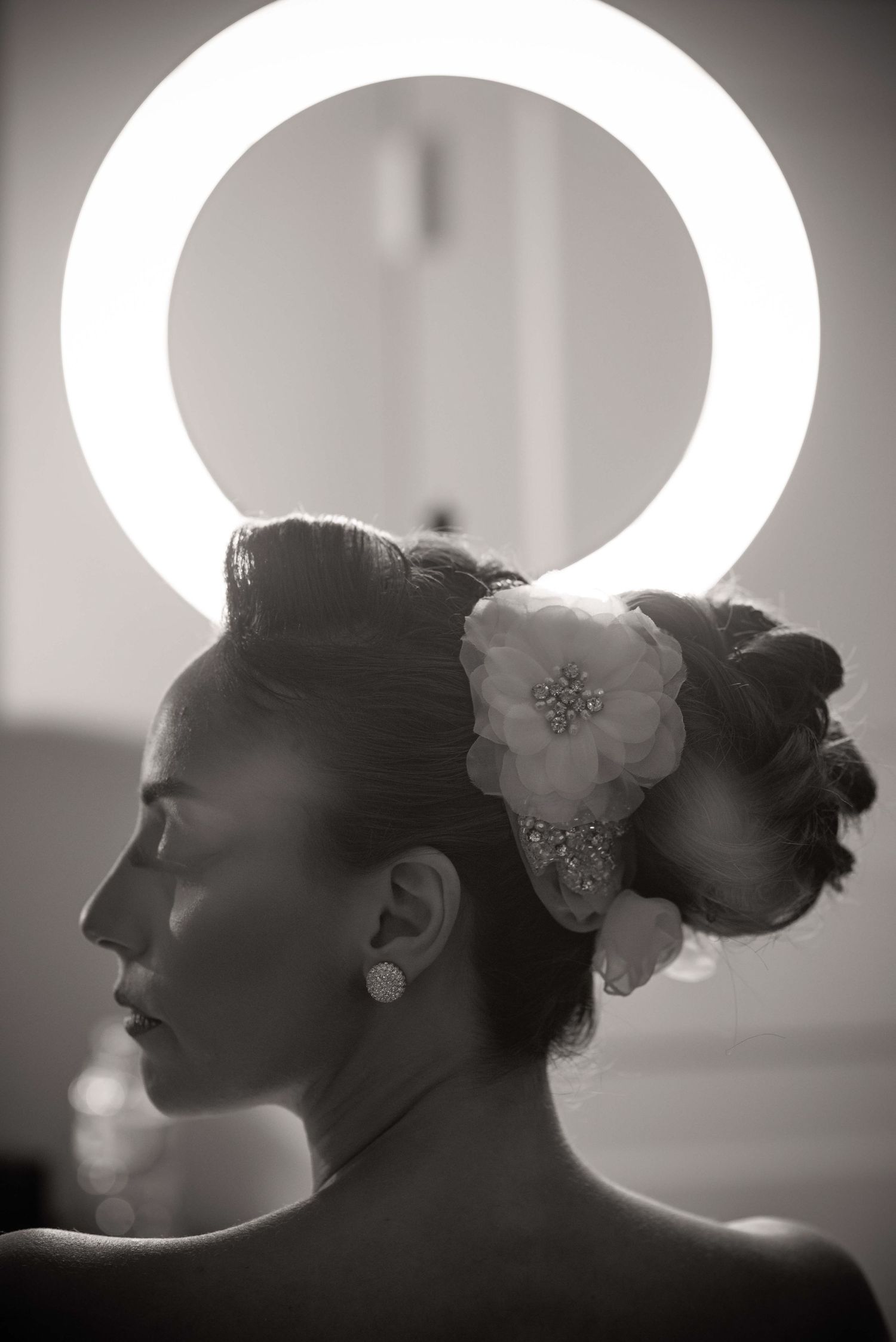 Black and white portrait of a bride with an elegant updo and floral hair accessory backlit by a circular light.